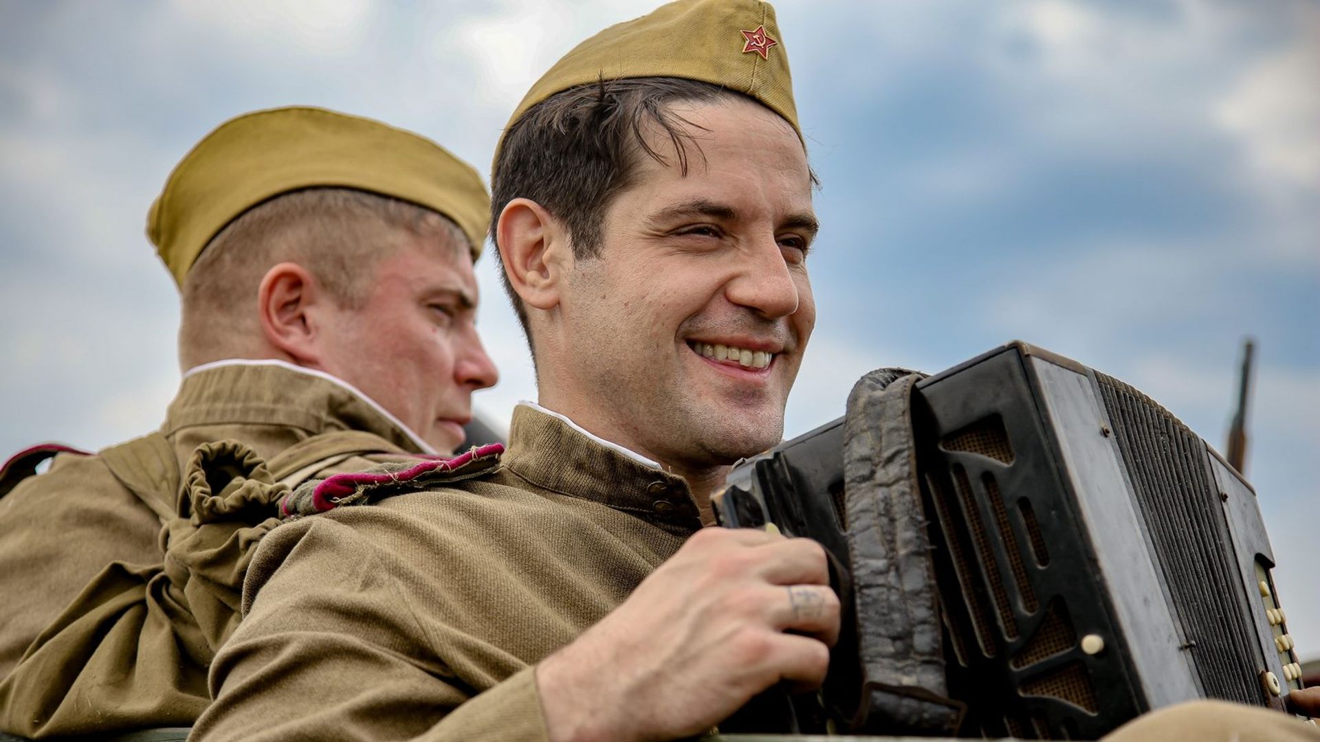 Марк Богатырёв в военной форме Второй мировой войны играет на гармони