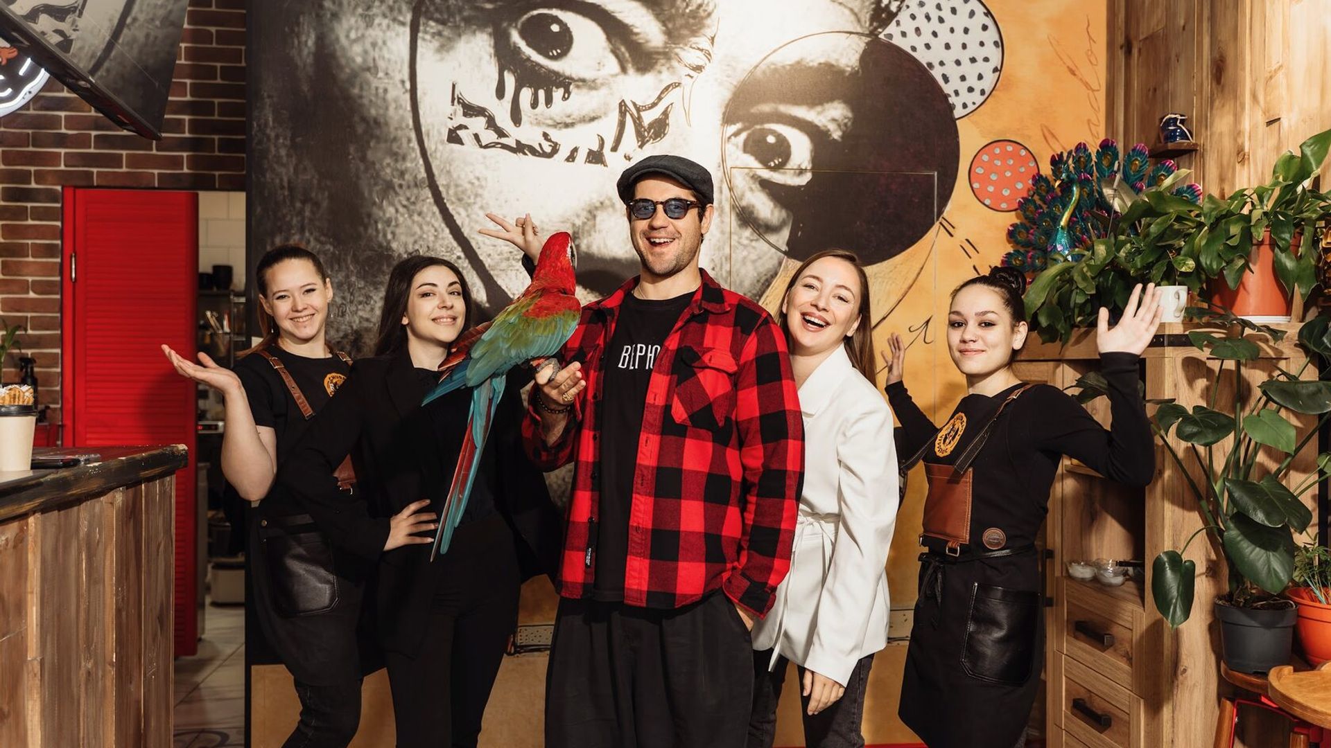 Марк Богатырёв держит в руках попугая ара, рядом в ряд стоят официантки