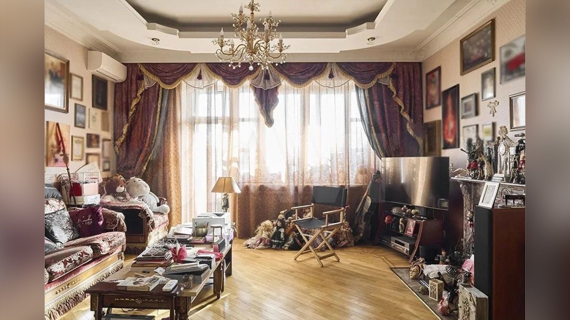 Просторная комната с паркетным полом, многоуровневым потолком и тяжёлыми шторами, на стенах множество картин