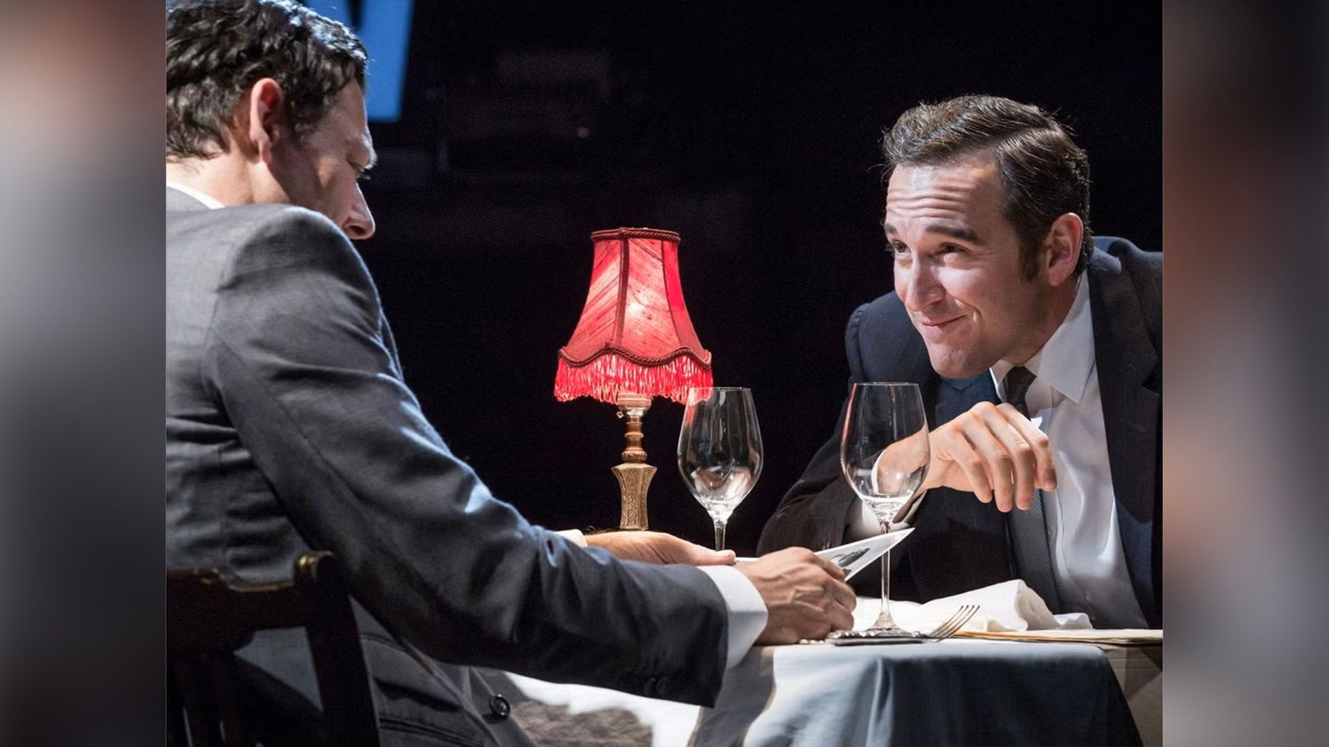 Берти Карвел сидит за столиком с красным светильником и двумя бокалами, с прищуром глядя на мужчину с газетой, сидящего напротив