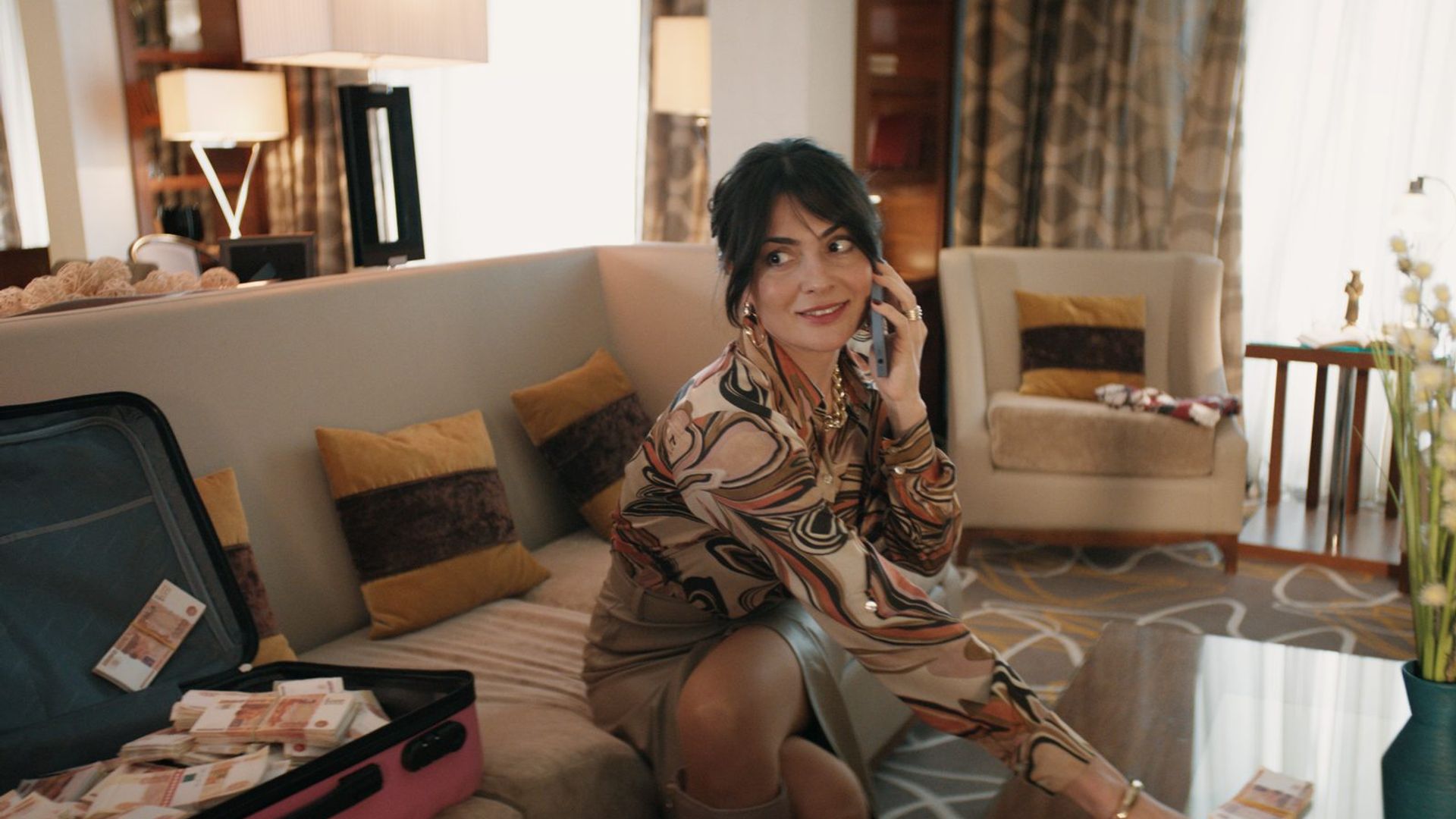 Виктория Полторак в платье сидит на диване и говорит по телефону