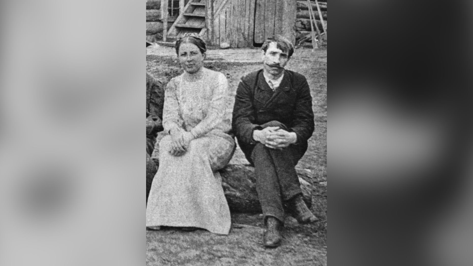 Александр Грин и Вера Абрамова сидят на бревне во дворе деревянного дома