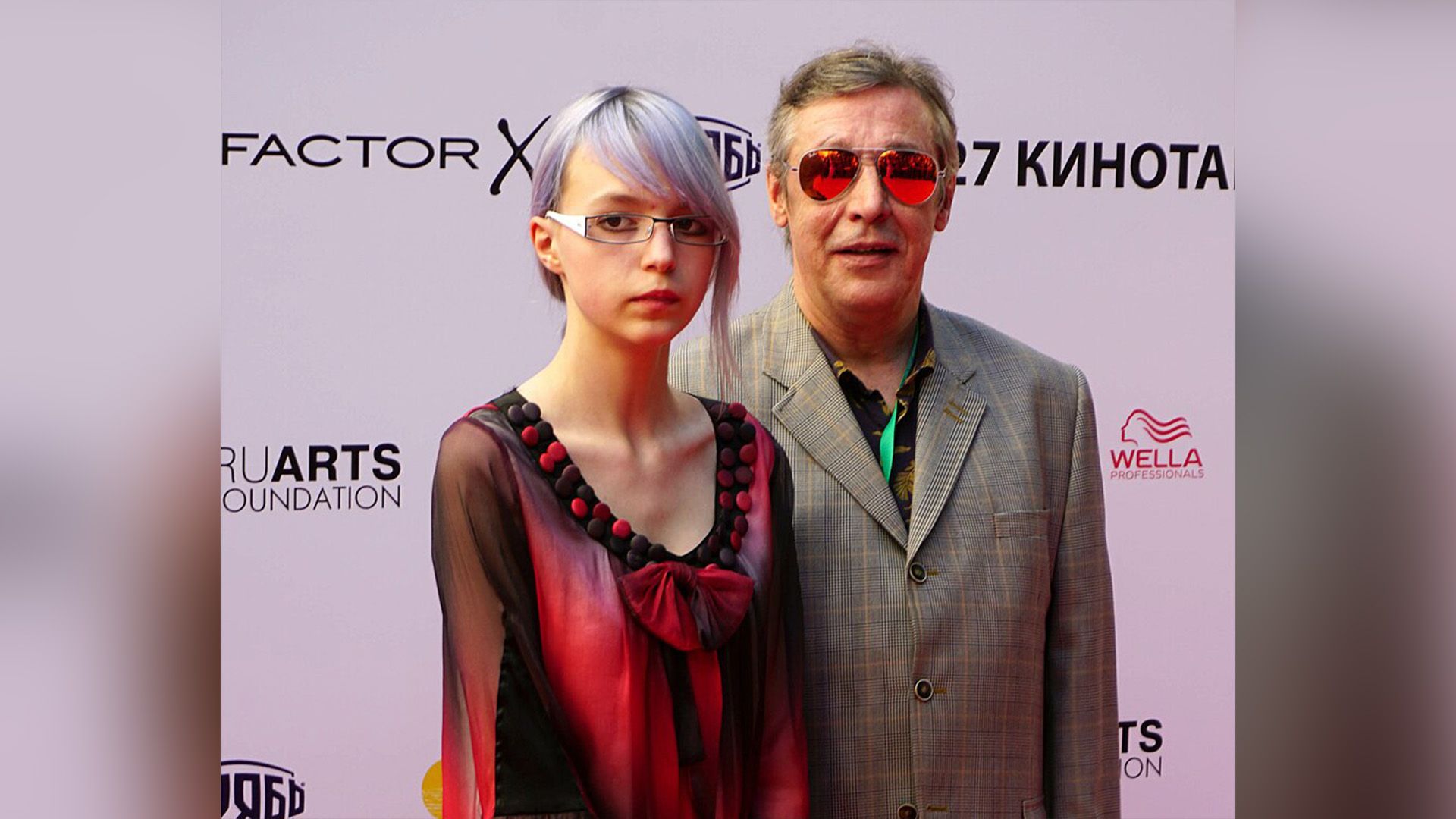 Михаил Ефремов в клетчатом сером пиджаке и тёмных очках и его дочь Анна-Мария в красно-фёрном платье