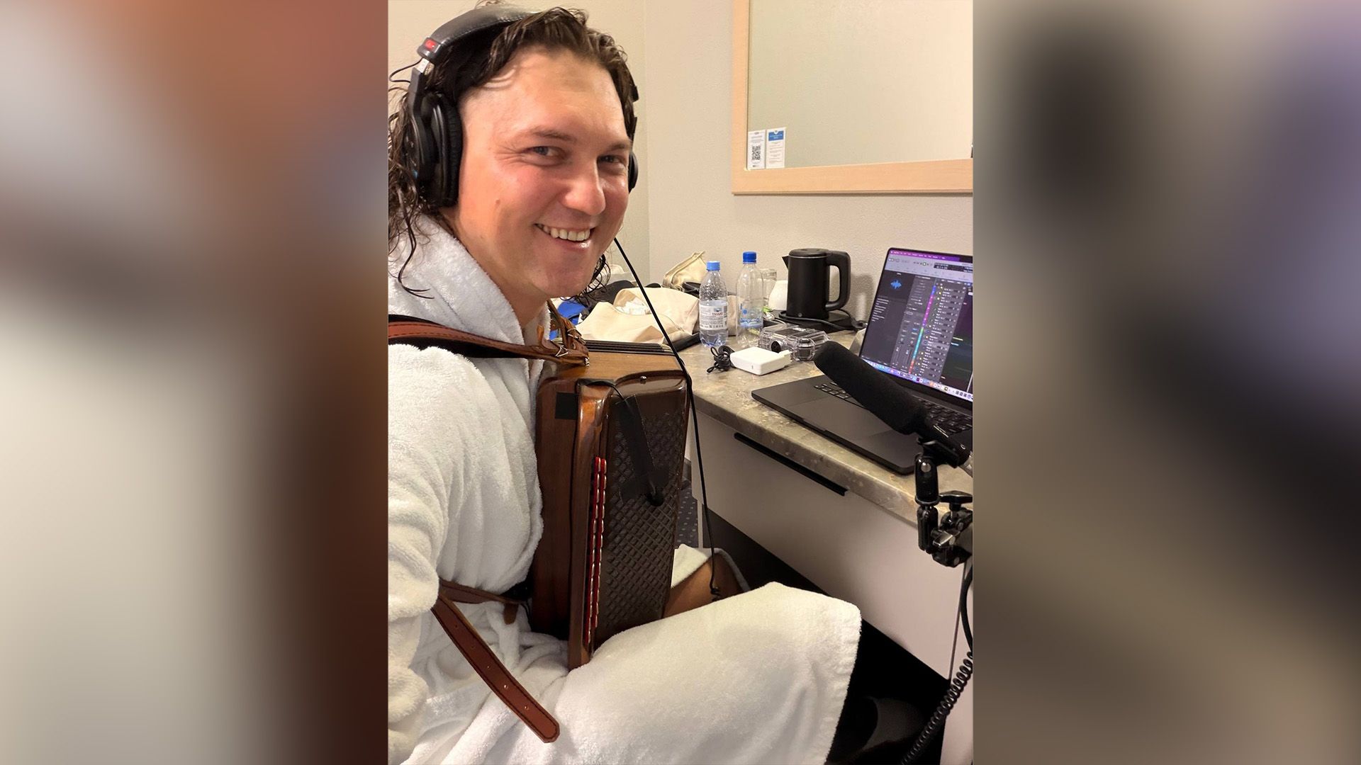 Александр Бардин в наушниках и с баяном сидит за ноутбуком в гостиничном номере