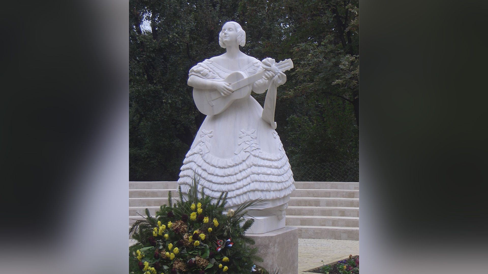 Белый памятник, изображающий Розу Дерине в пышном платье, играющую на гитаре