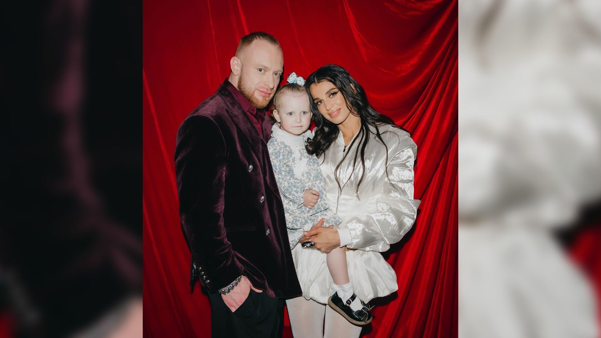 Лёша Свик, Ксения Ткачёва и их дочь Эмилия в нарядных одеждах позируют на бордовом фоне