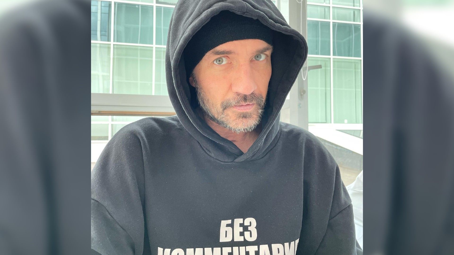 Роман Костомаров в чёрном худи смотрит в камеру