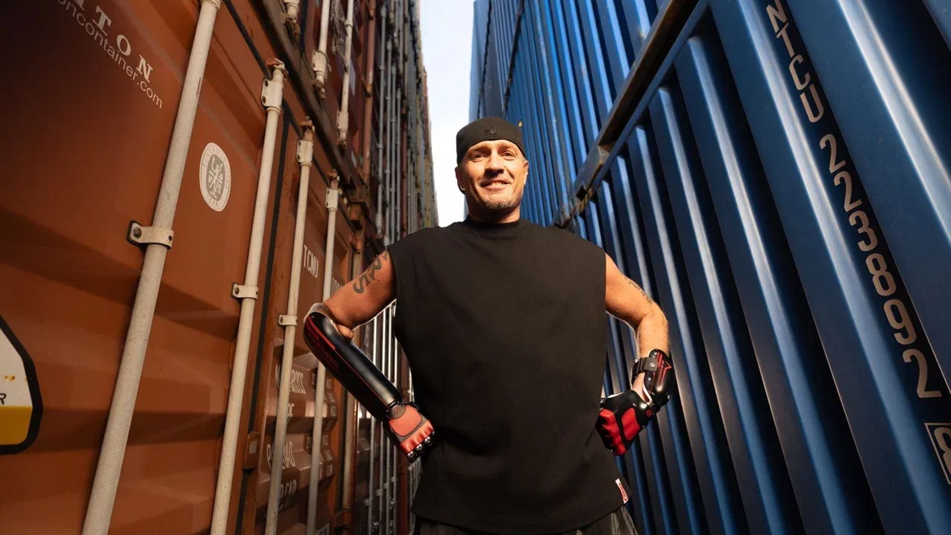 Роман Костомаров стоит, уперев руки в бок, на фоне контейнеров