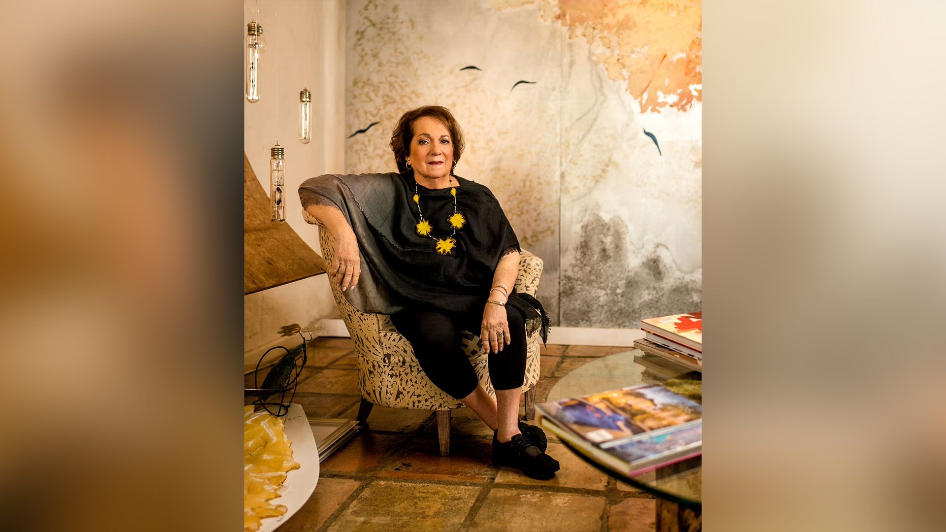 Художница Мира Лер, одетая в чёрное, сидит в кресле в своей студии