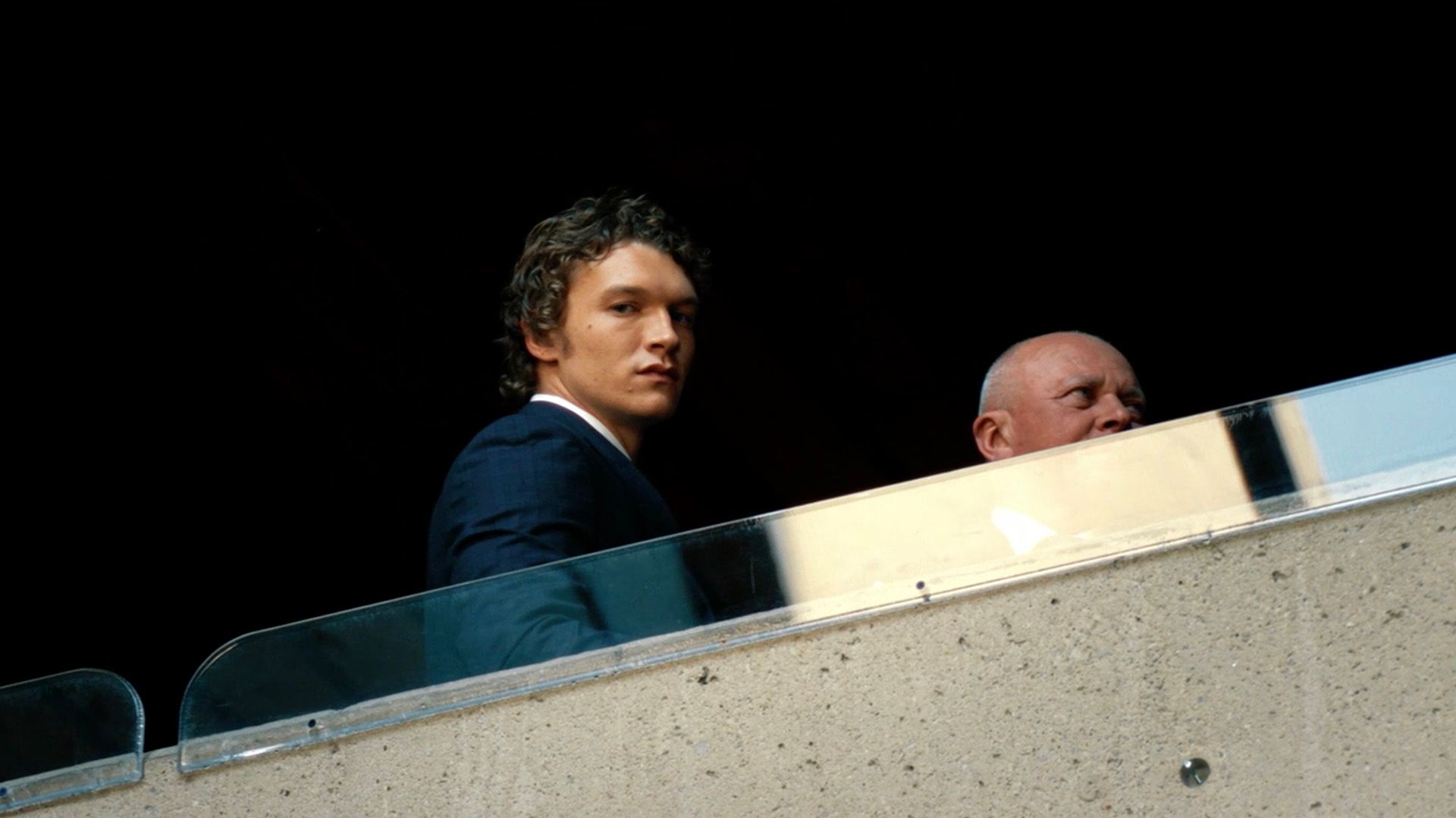 Коннор Сторри в пиджаке задумчиво смотрит вниз с балкона