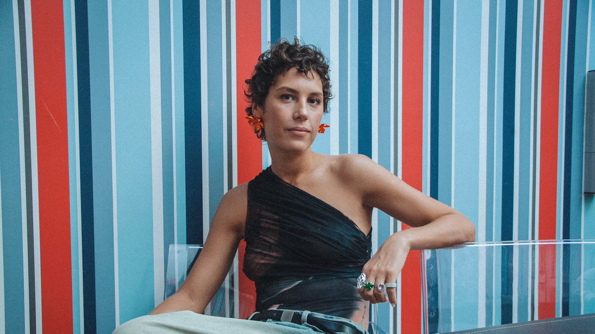 Ирина Горбачёва сидит за столом на фоне полосатых обоев