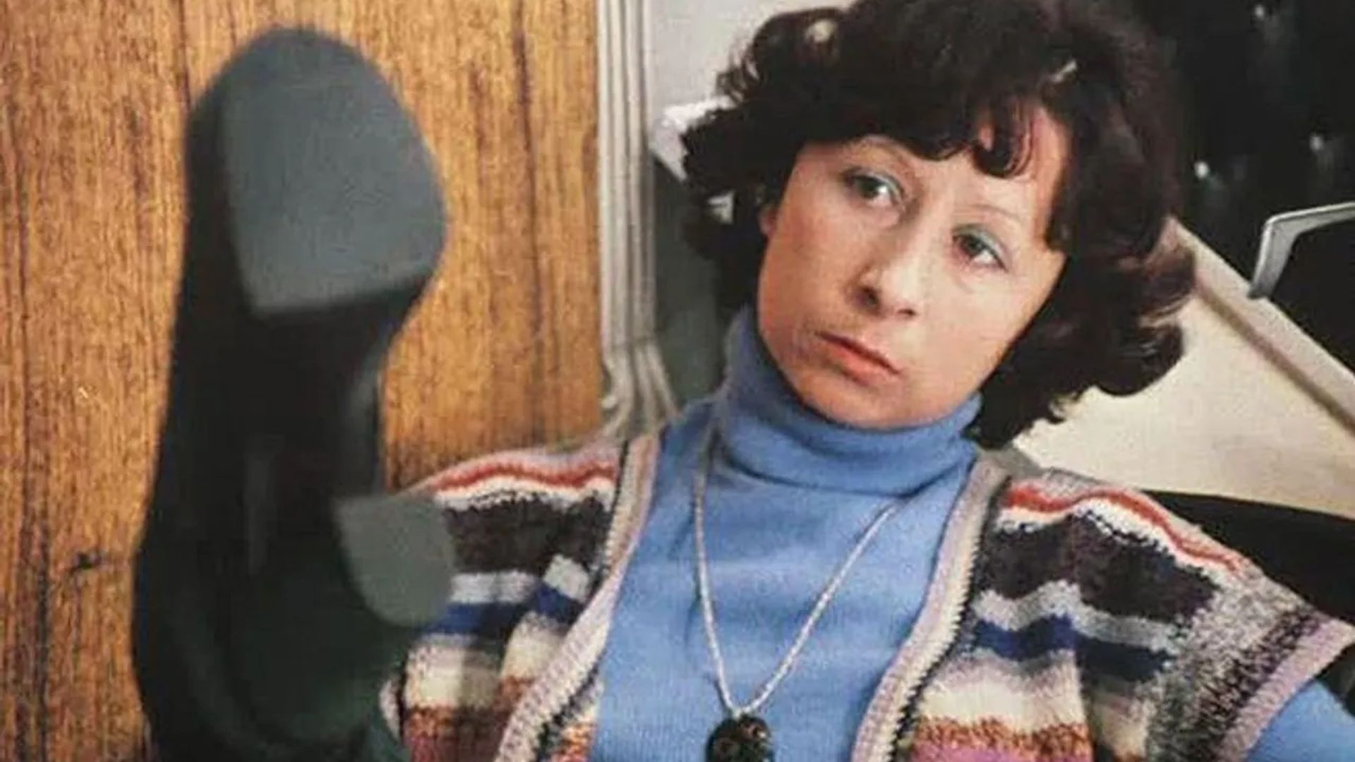 Лия Ахеджакова сидит за столом, рассматривая ногу в сапоге