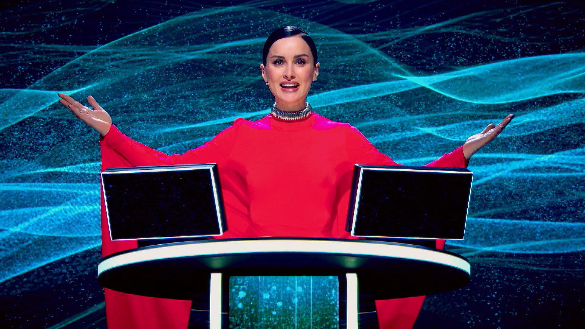 Тина Канделаки в красном платье стоит, разведя руки, на трибуне