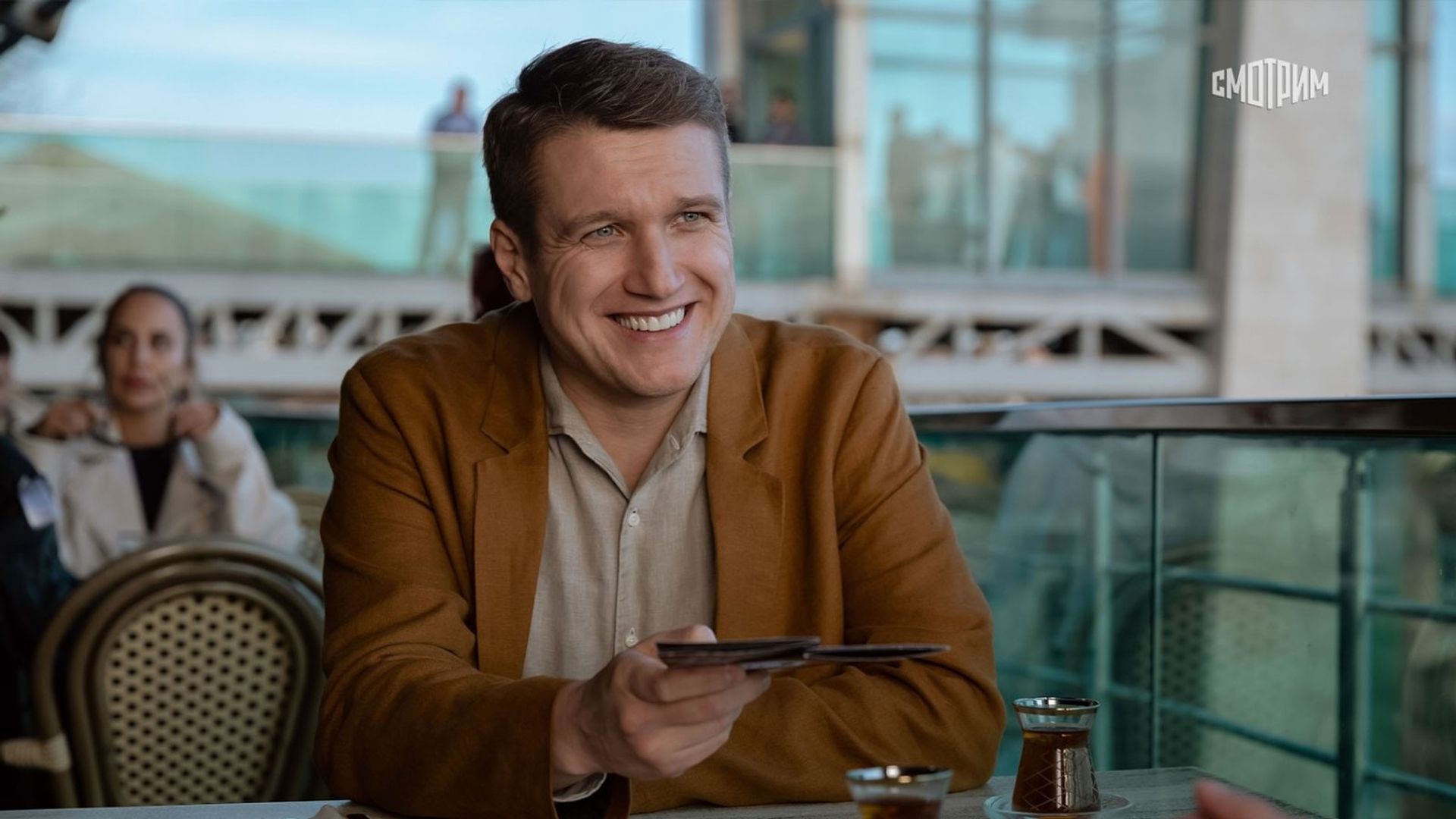 Анатолий Руденко в коричневом пиджаке улыбается за столиком в ресторане