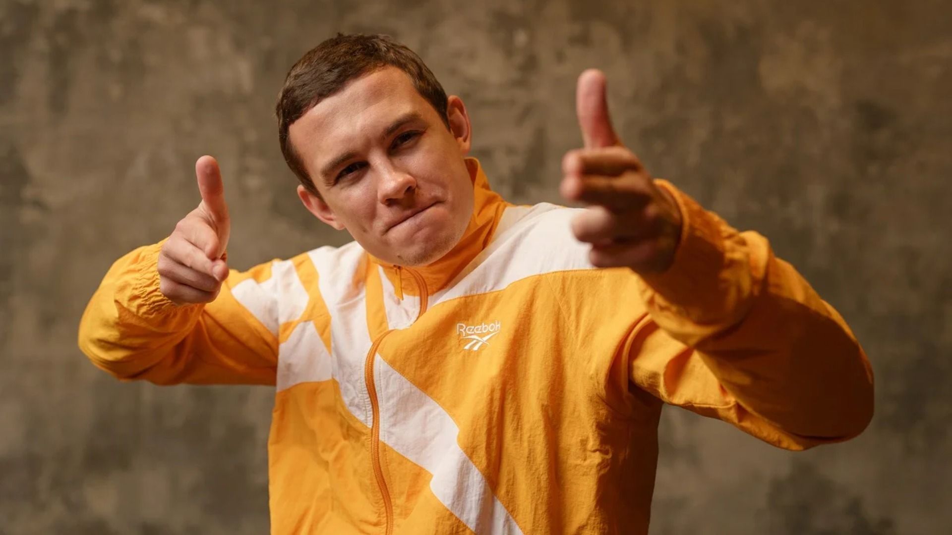 Актер Никита Кологривый в спортивном костюме выставил указательные пальцы вперед