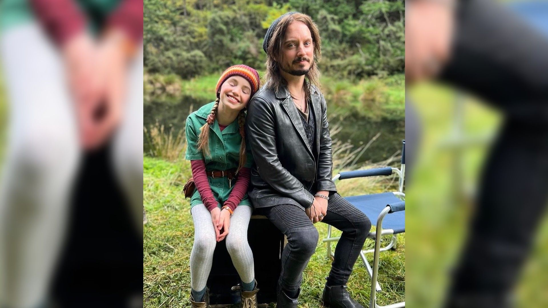 Нелл Фишер и Элайджа Вуд сидят на одном стуле на природе и улыбаются