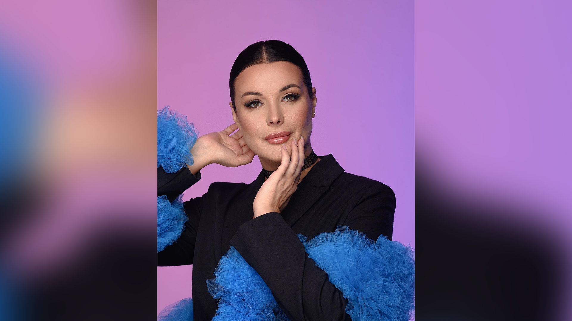 Оксана Фёдорова в черном пиджаке с синим кружевным боа на фиолетовом фоне
