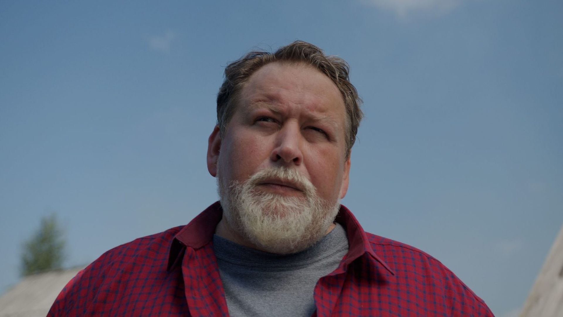 Станислав Дужников в клетчатой рубашке и с бородой смотрит выше камеры