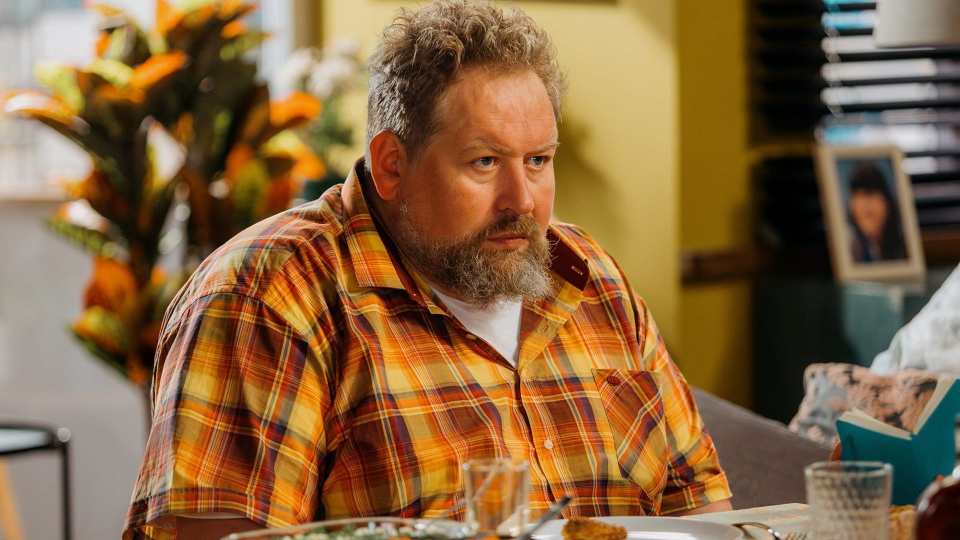 Станислав Дужников в оранжевой клетчатой рубашке и с кустистой бородой сидит на столом