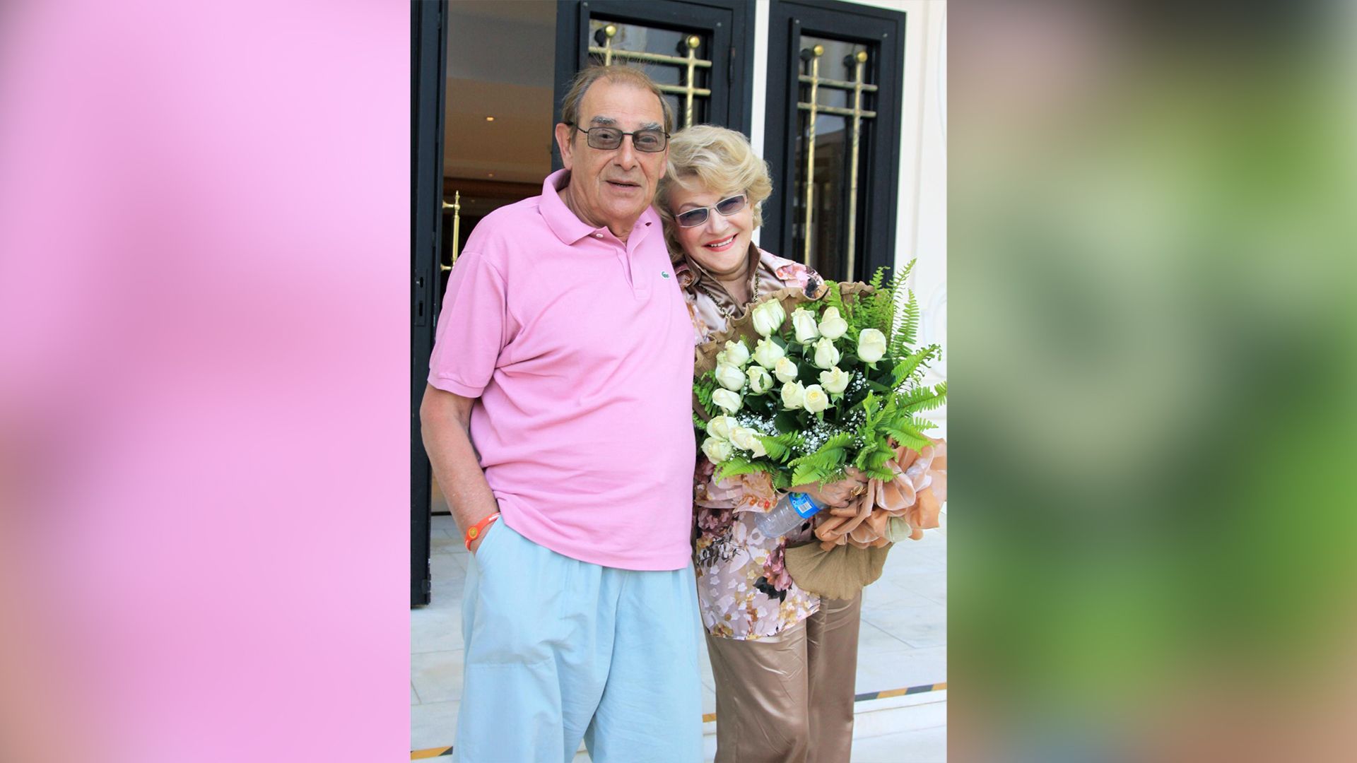 Анатолий Мукасей в голубых шортах и розовом поло и Светлана Дружинина с букетом белых роз