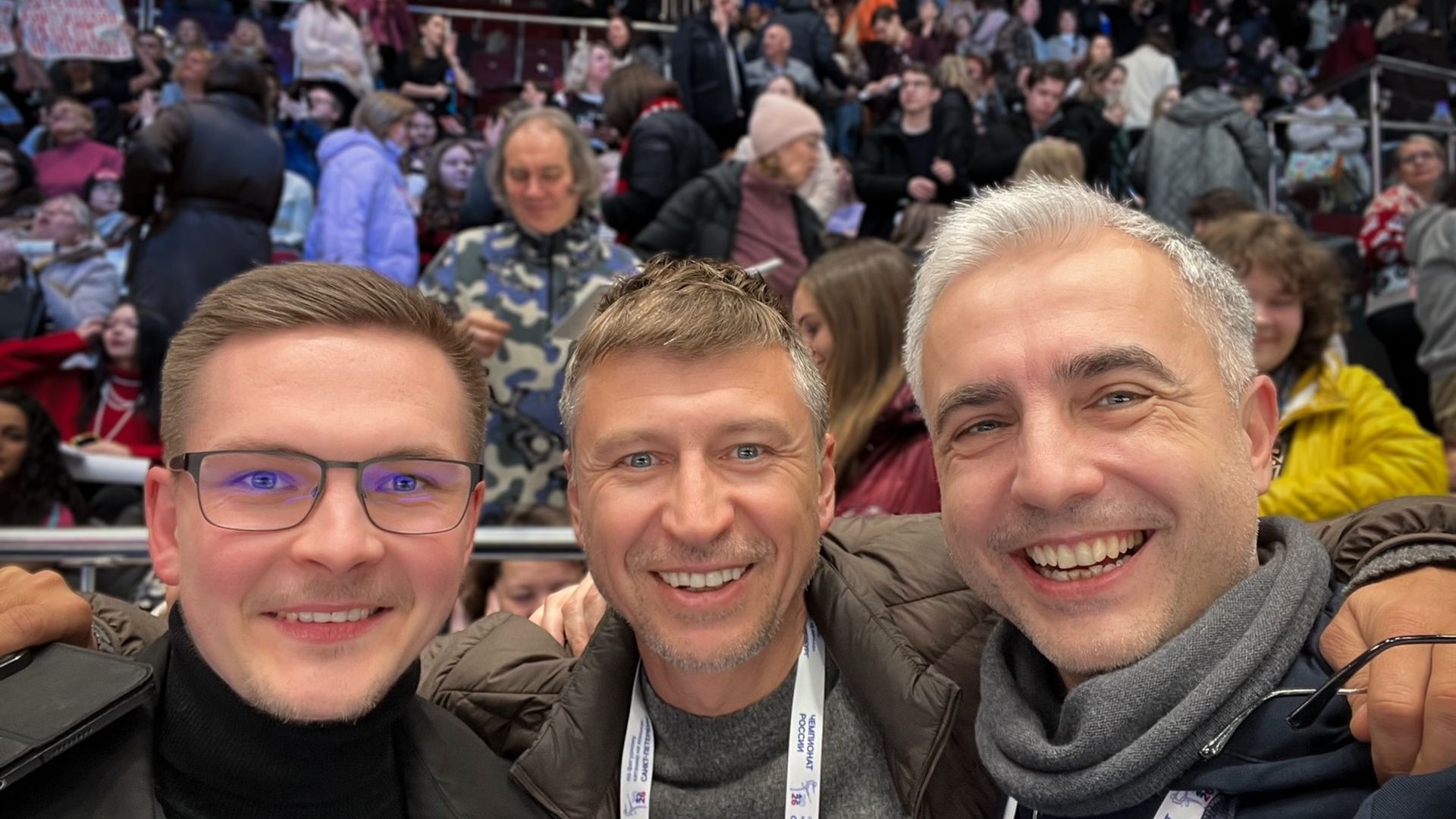 Михаил Коляда, Алексей Ягудин и Василий Соловёьв улыбаются на фоне спортивных трибун