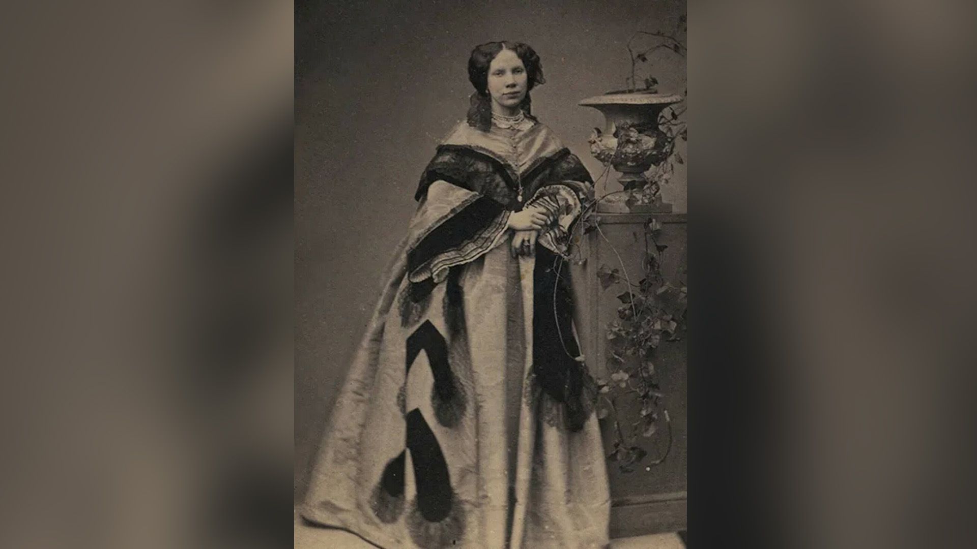 Мария Боткина позирует, стоя у колонны с вазоном с цветами