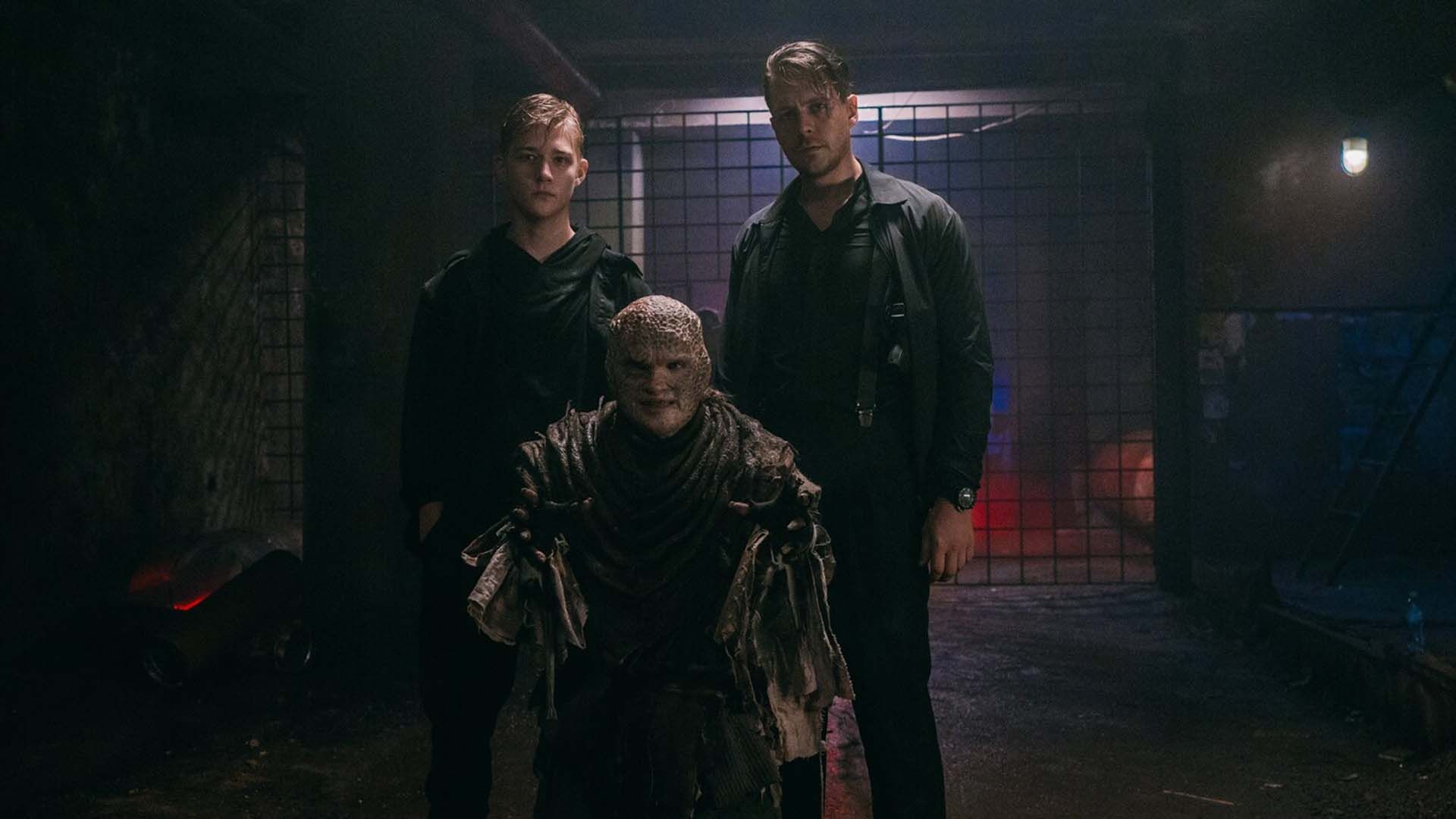 Олег Савостюк и Милош Бикович стоят рядом с человеком в гриме монстра в тёмном подвале