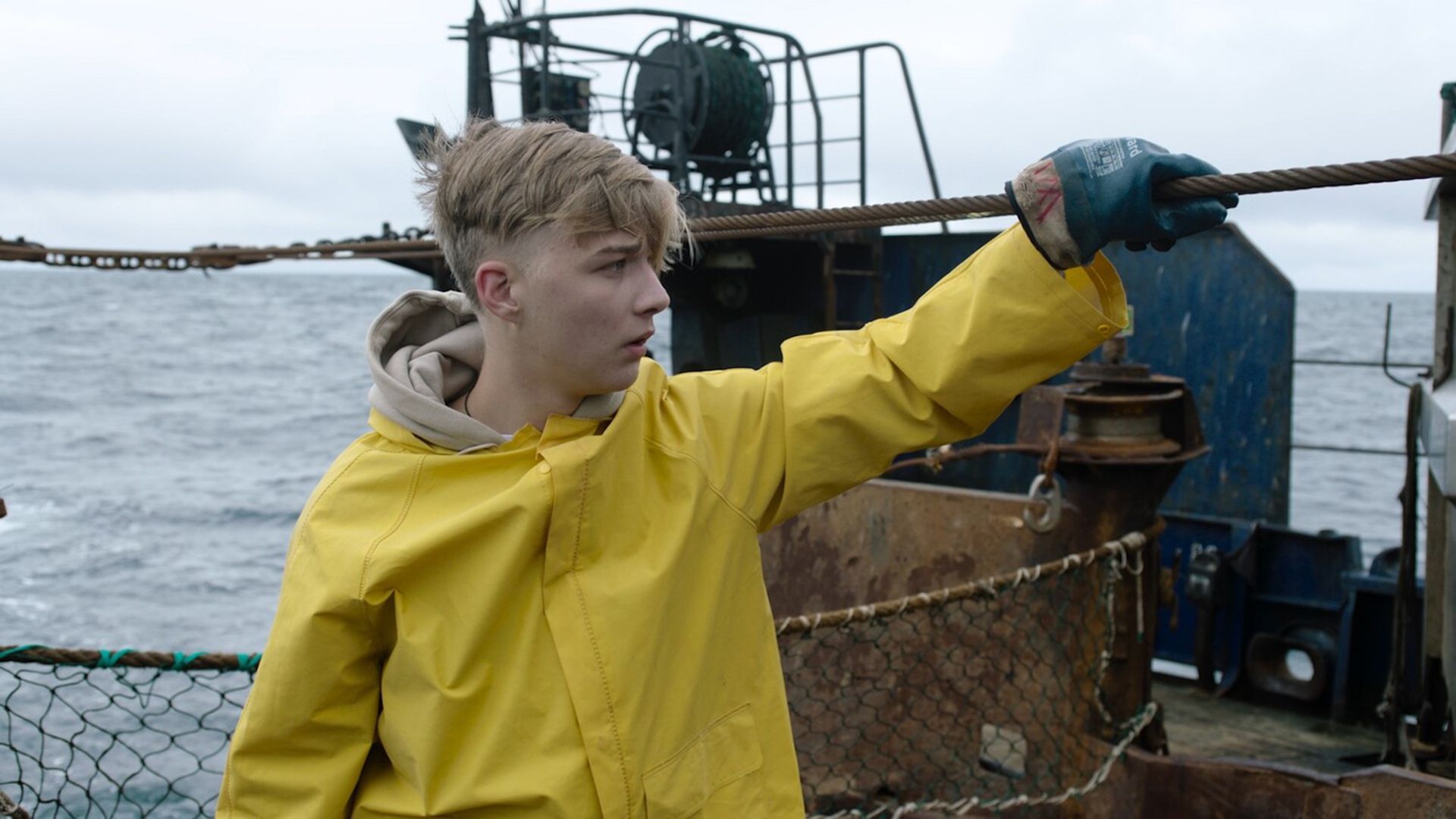 Олег Савостюк в желтом дождевике стоит на борту ржавого судна