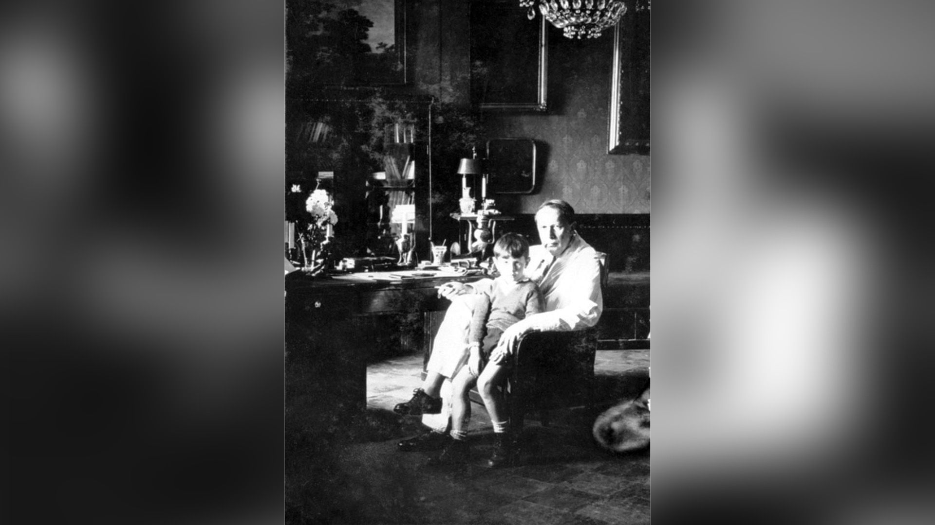 Алексей Толстой сидит в кресле в кабинете, рядом с ним стоит маленький Никита Толстой