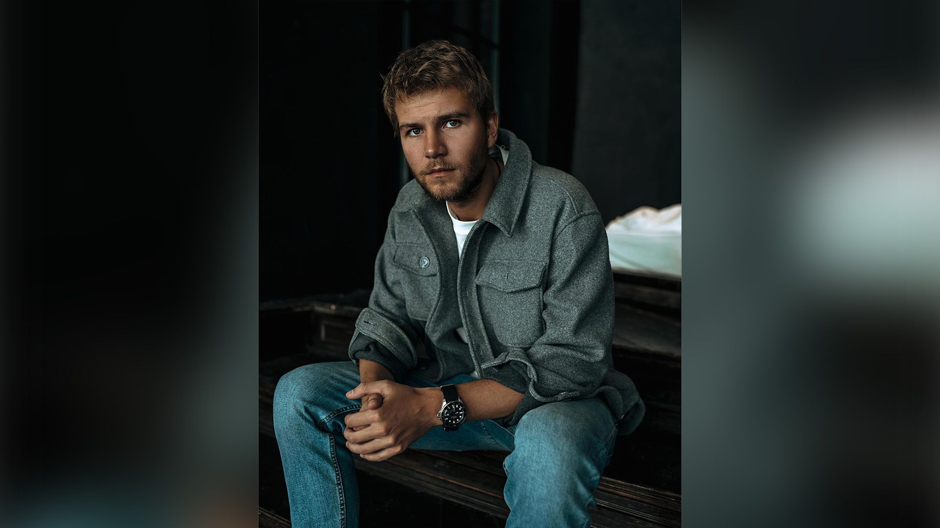 Актёр Арсений Робак в сером пальто и голубых джинсах