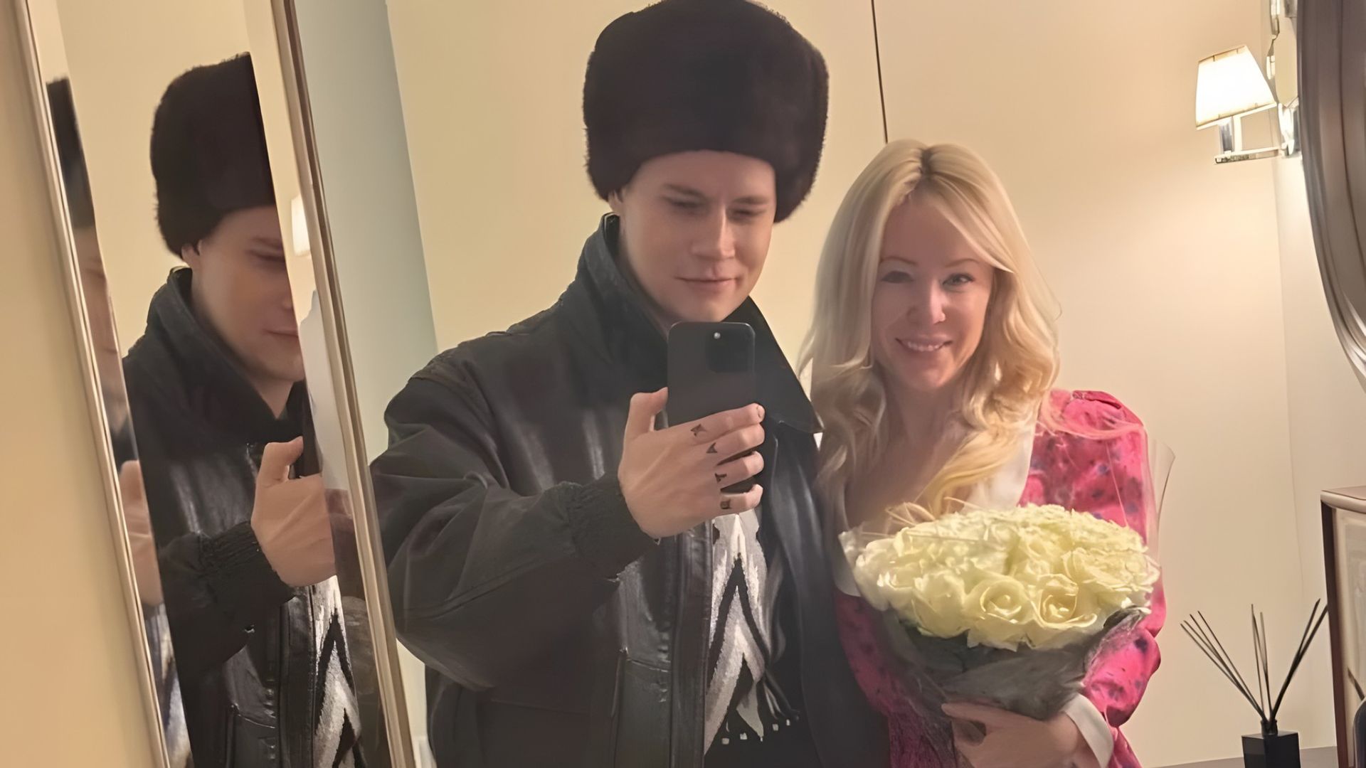 Мужчина в меховой шапке и женщина с розовом платье с букетом белых роз фотографируются