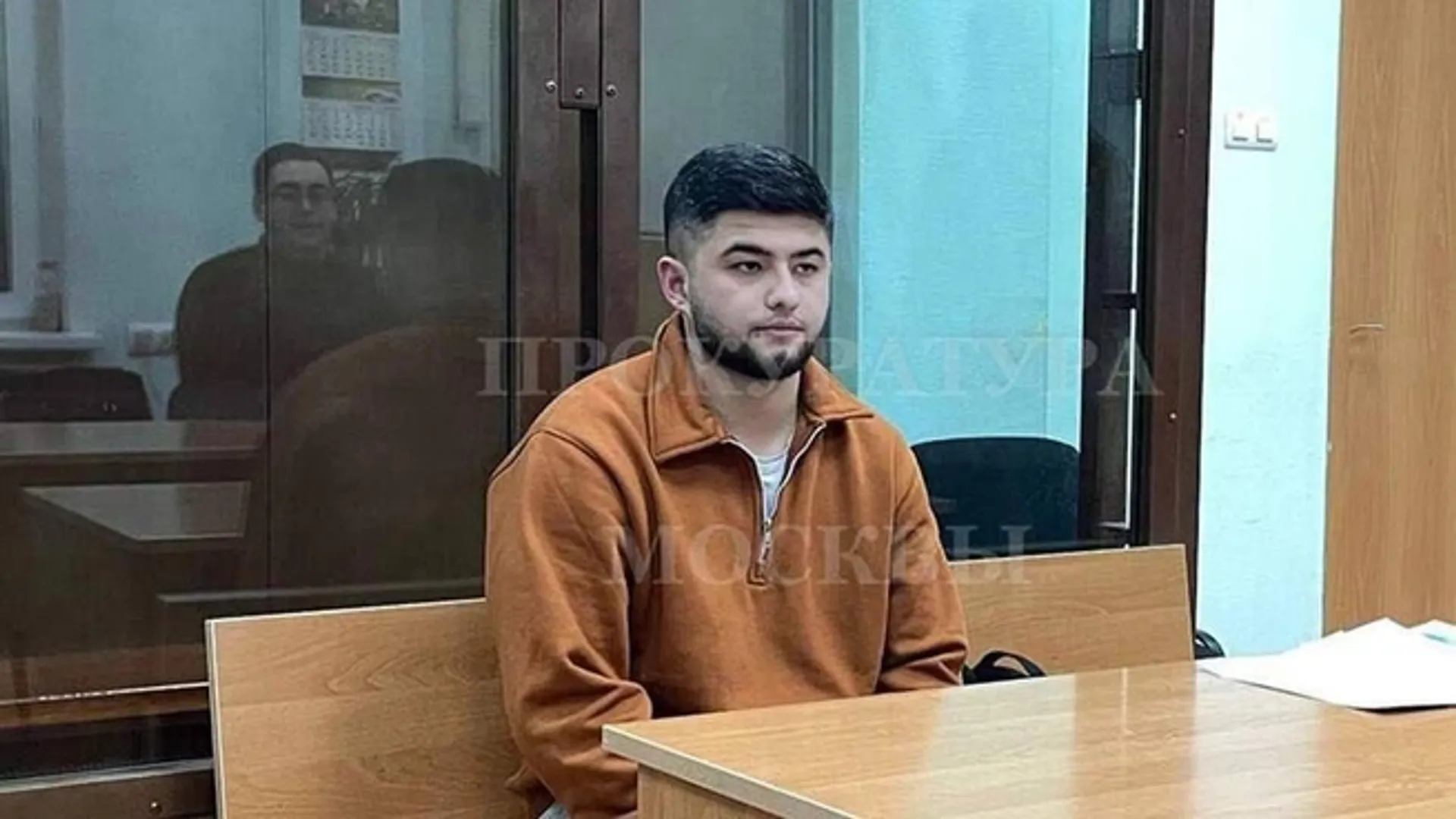 Мужчина в коричневой толстовке сидит в зале суда