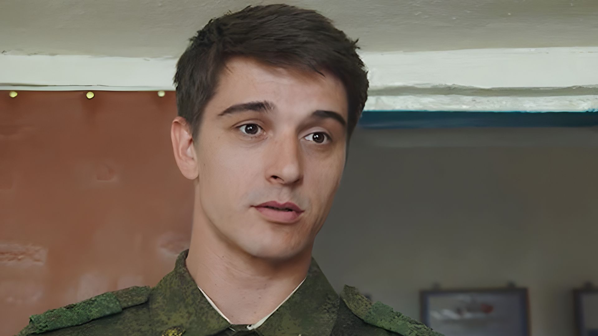 Станислав Бондаренко в военной форме стоит в помещении и смотрит вперёд с серьёзным выражением лица