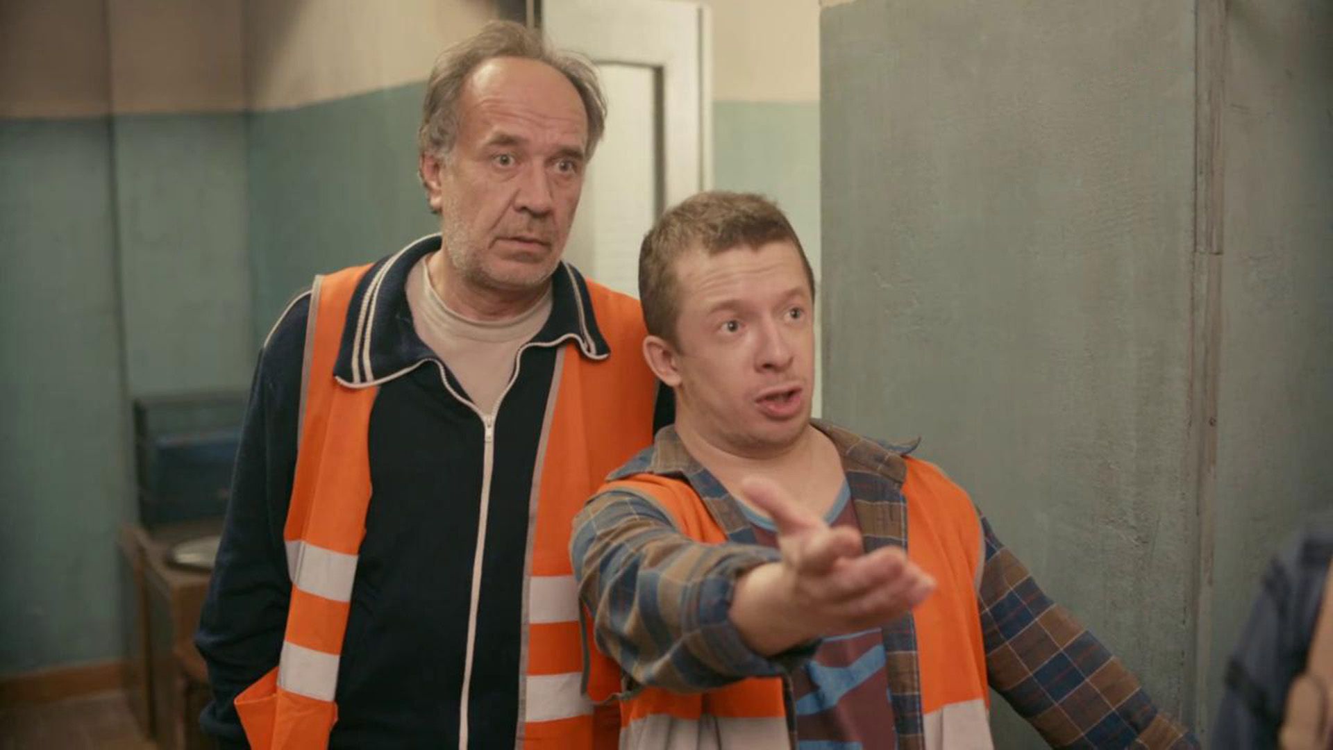 Тимофей Зайцев вытянул вперед руку с возмущённым выражением лица, рядом стоит мужчина в возрасте, оба в оранжевых жилетах рабочих