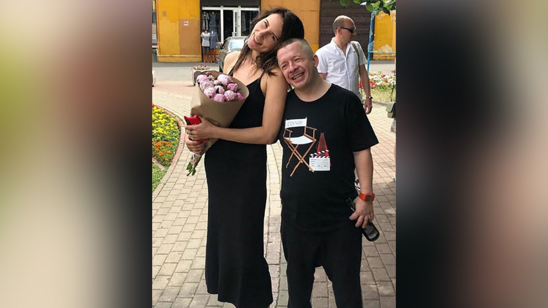 Тимофей Зайцев в чёрном стоит рядом с женой Екатериной, держащей в руках букет цветов