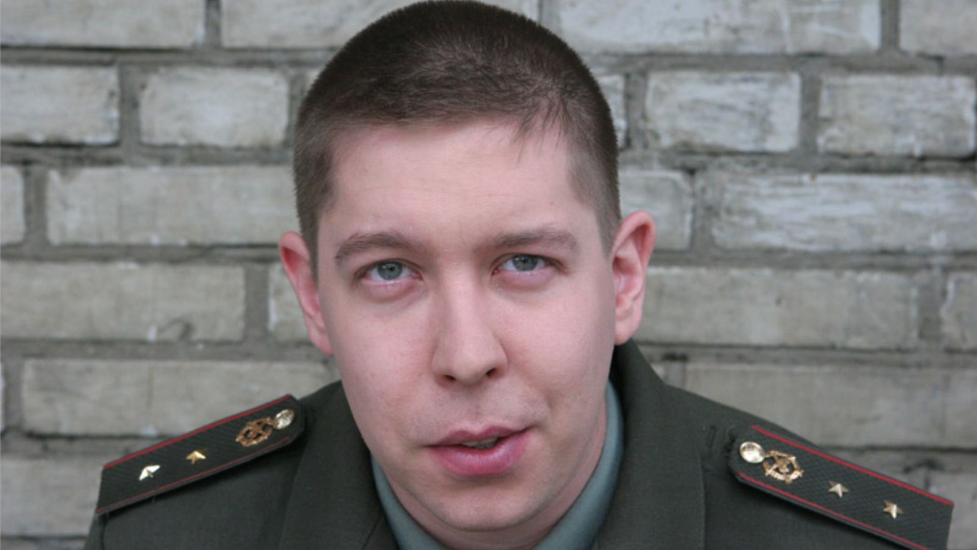 Актер Иван Моховиков в военной форме смотрит в камеру на фоне кирпичной стены