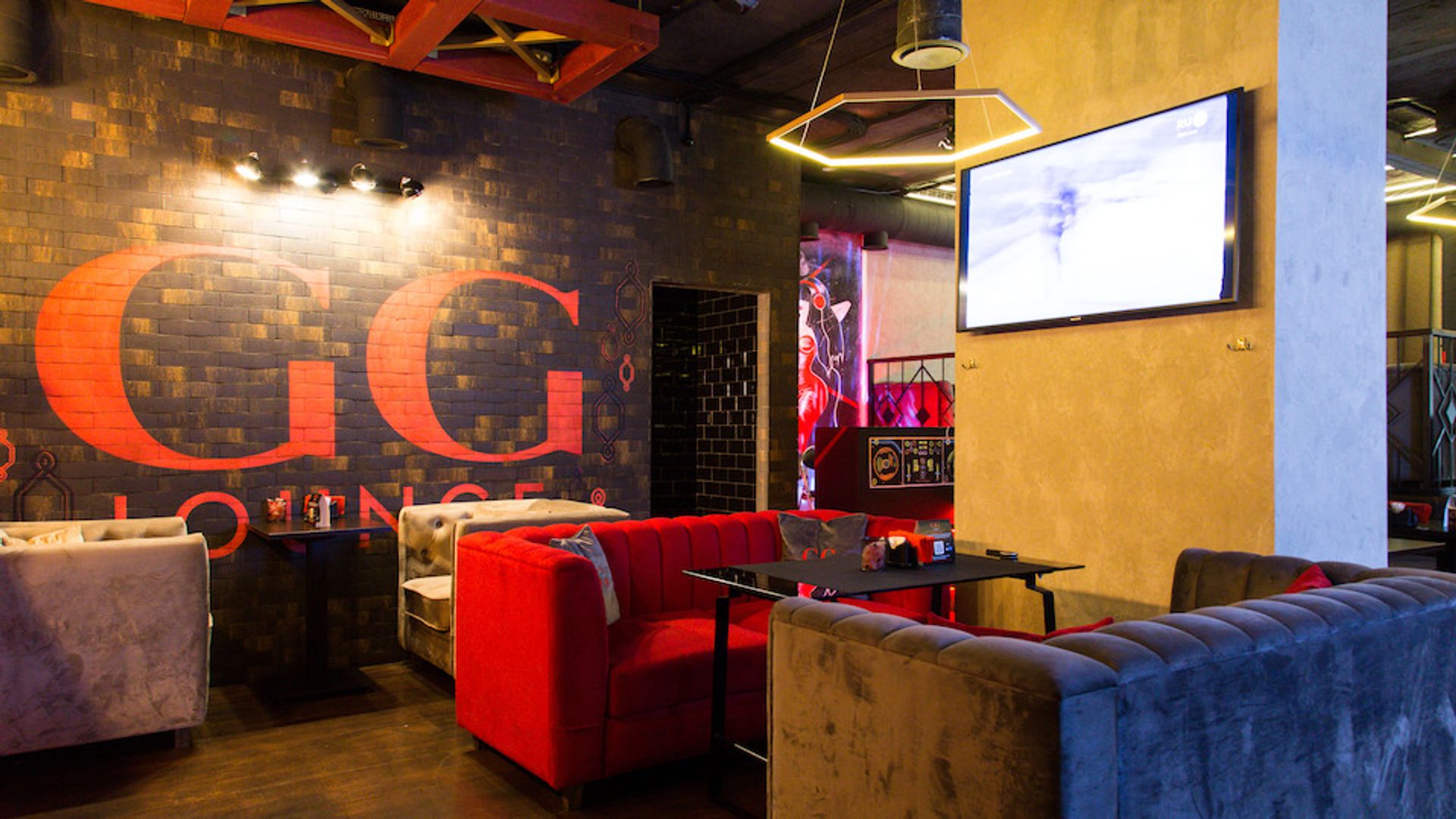 Интерьер лаунж-бара GG Lounge с мягкими диванами, телевизором на стене и надписью на кирпичной кладке