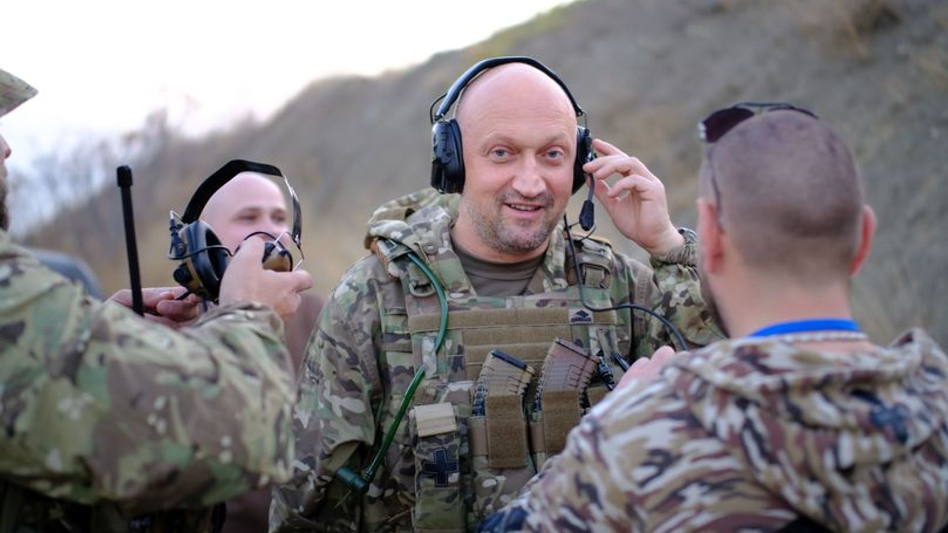 Гоша Куценко в военной форме с наушниками и микрофоном, вокруг него несколько человек в камуфляже