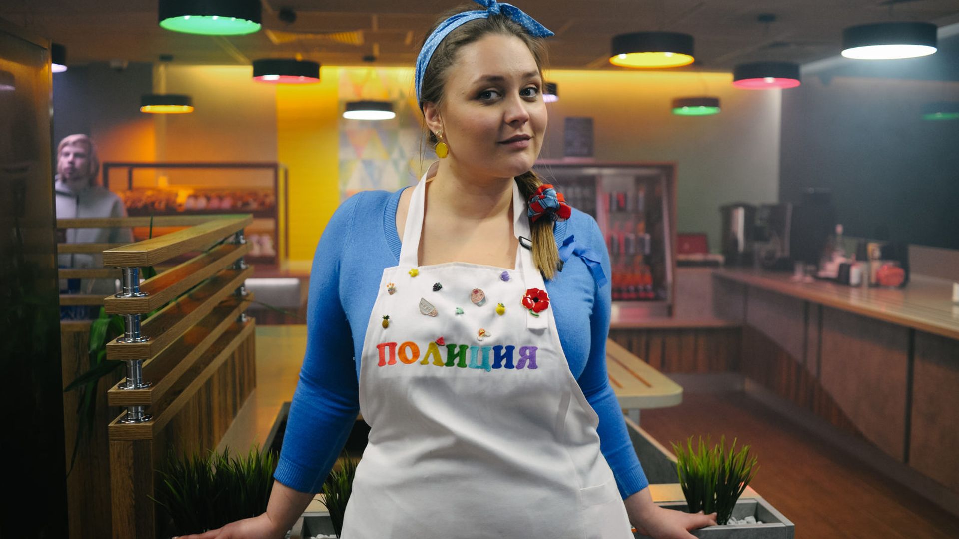 Софья Зайка в фартуке с надписью «полиция» стоит в ярко освещённой закусочной