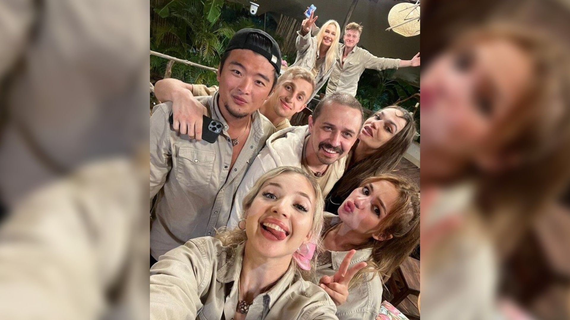 Группа улыбающихся молодых людей в бежевой одежде делает селфи на фоне зелени и декораций