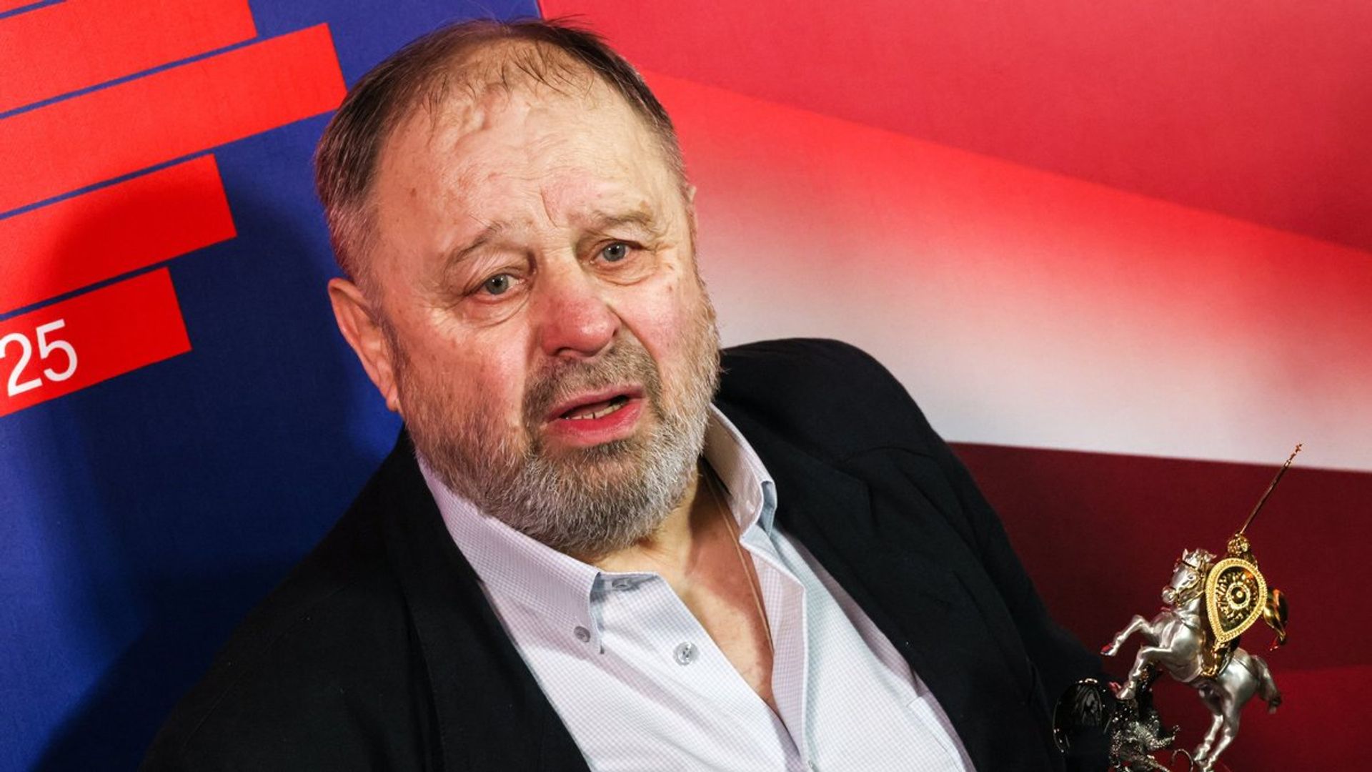 Владимир Ильин держит в руке кинопремию в виде всадника на фоне красно-синего баннера
