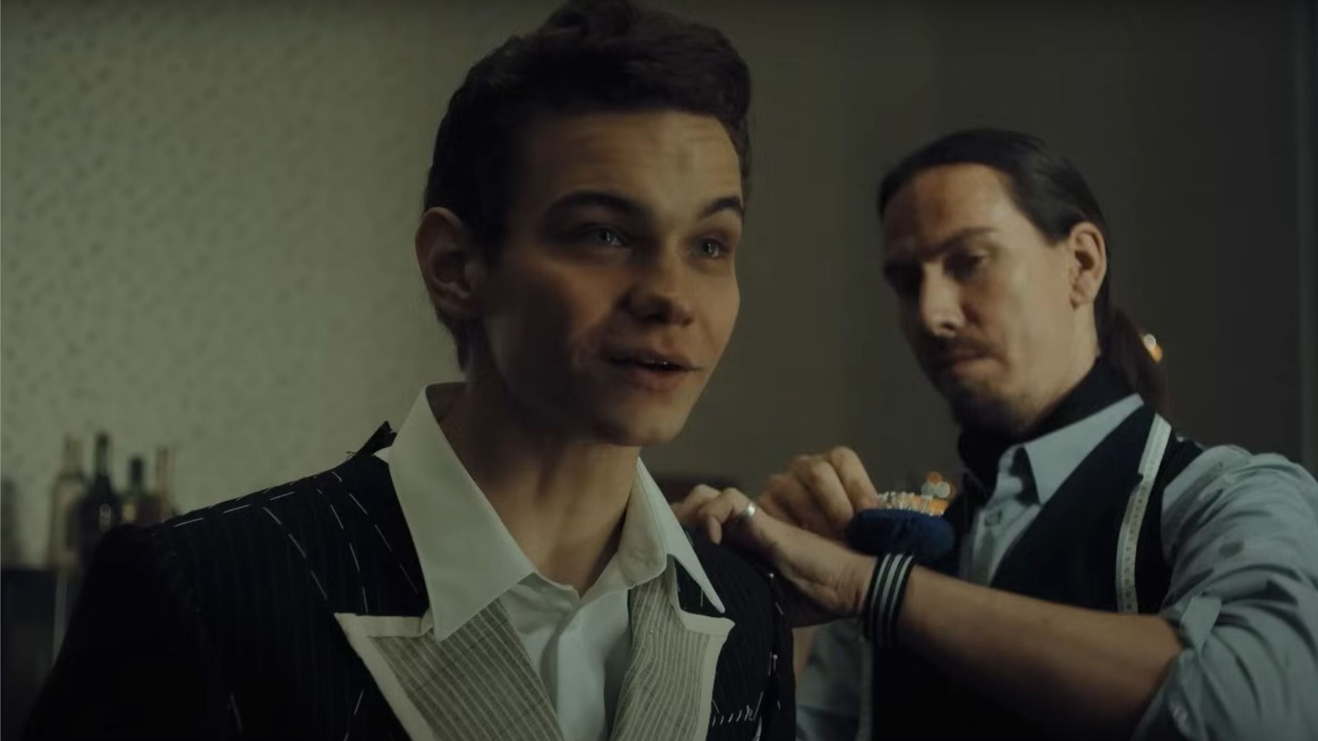 Актер Слава Копейкин стоит в костюме и улыбается на фоне стены, подняв одну бровь