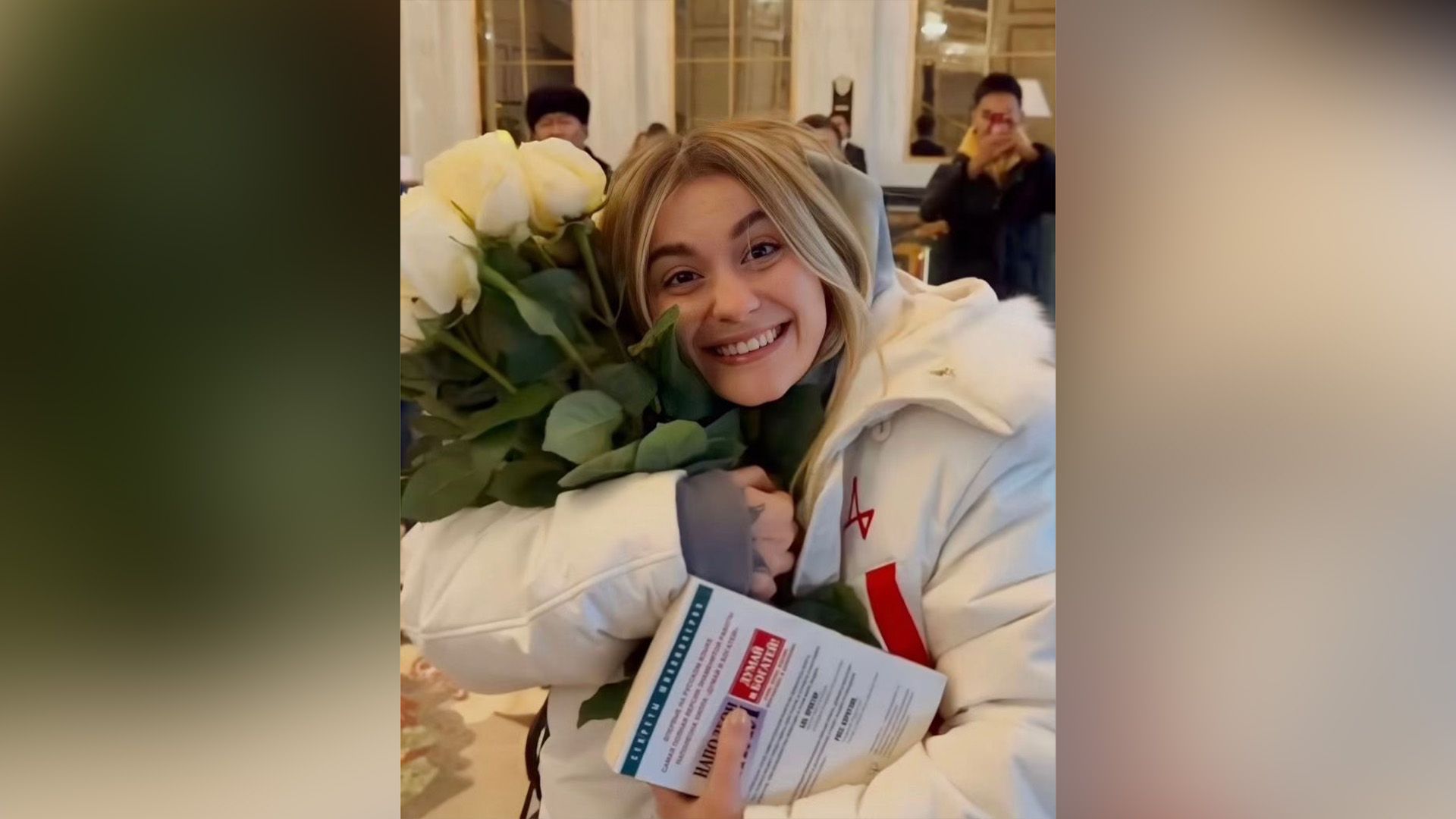 Светловолосая Дарья Кустовская в белой куртке прижимает к себе букет белых роз