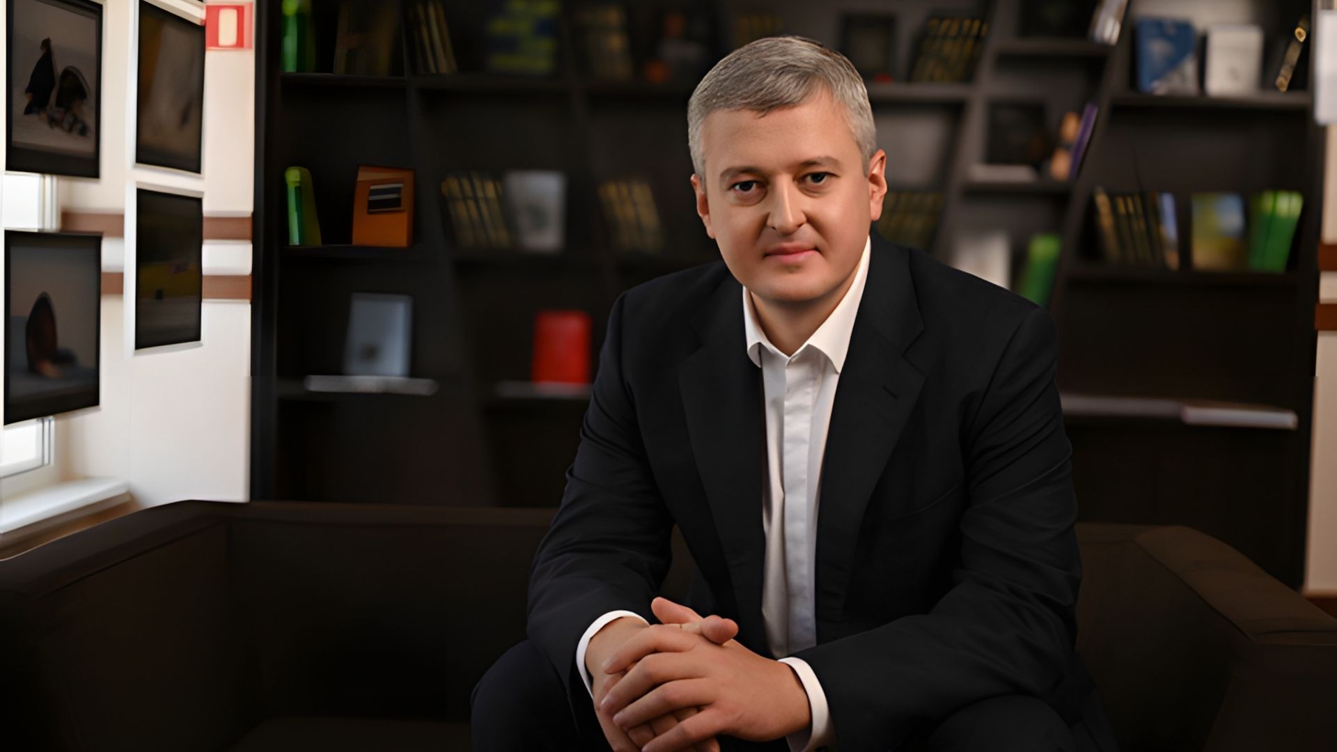 Владимир Солодов в официальном костюме сидит на диване на фоне кабинета