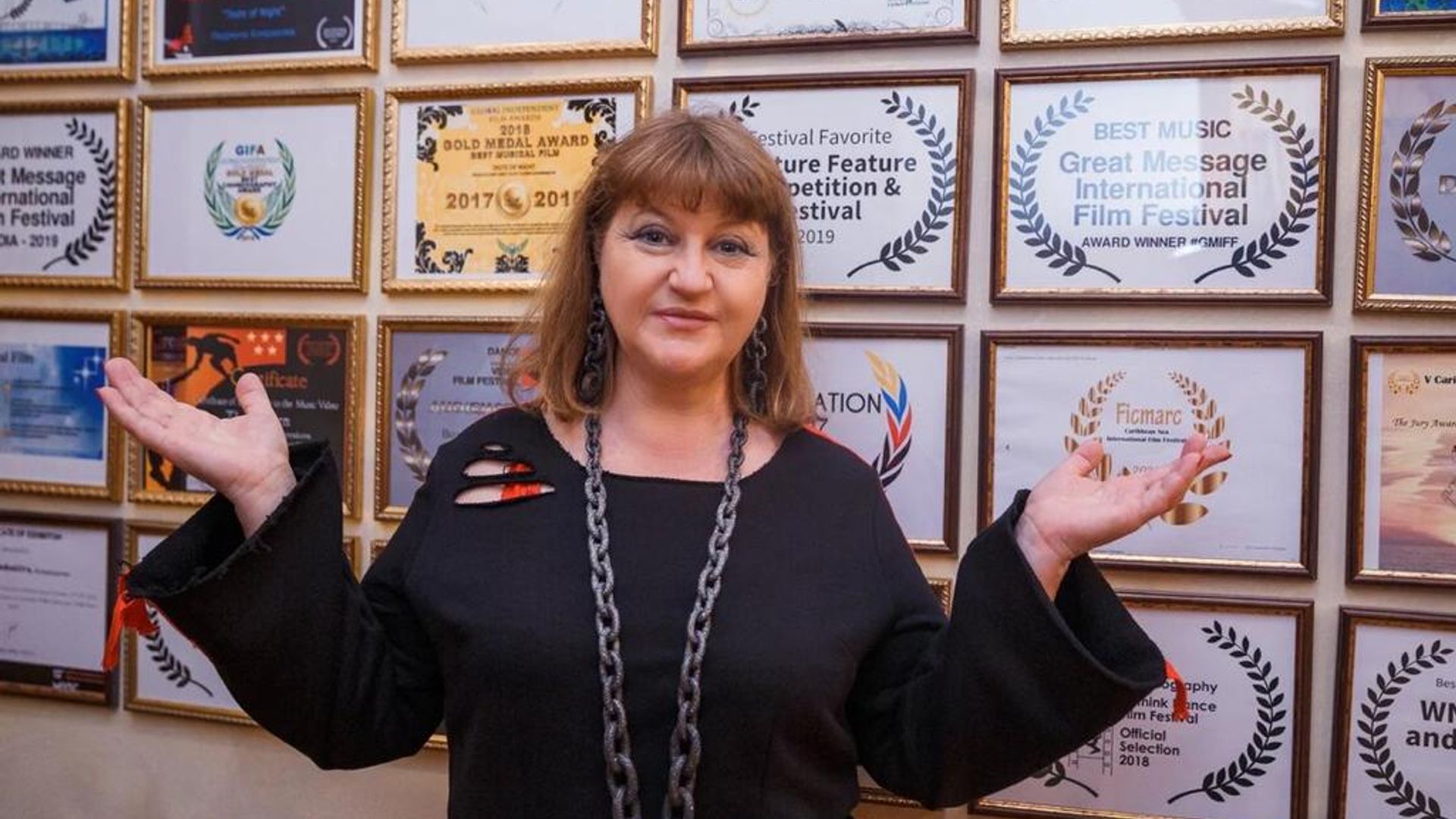 Режиссер Мила Комракова стоит на фоне дипломов от различных кинофестивалей