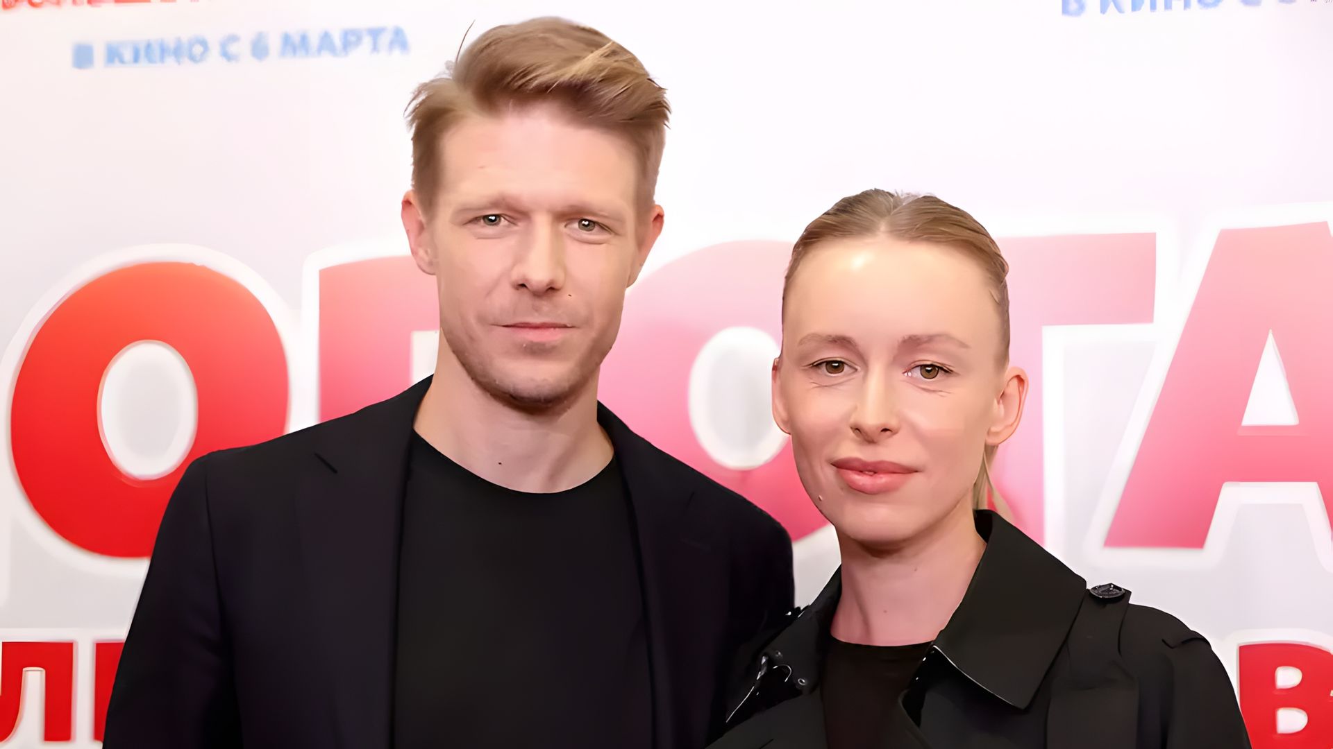 Никита Ефремов и Ольга Шурыгина позируют вместе на фоне постера с надписью, одеты в чёрное, смотрят прямо в камеру