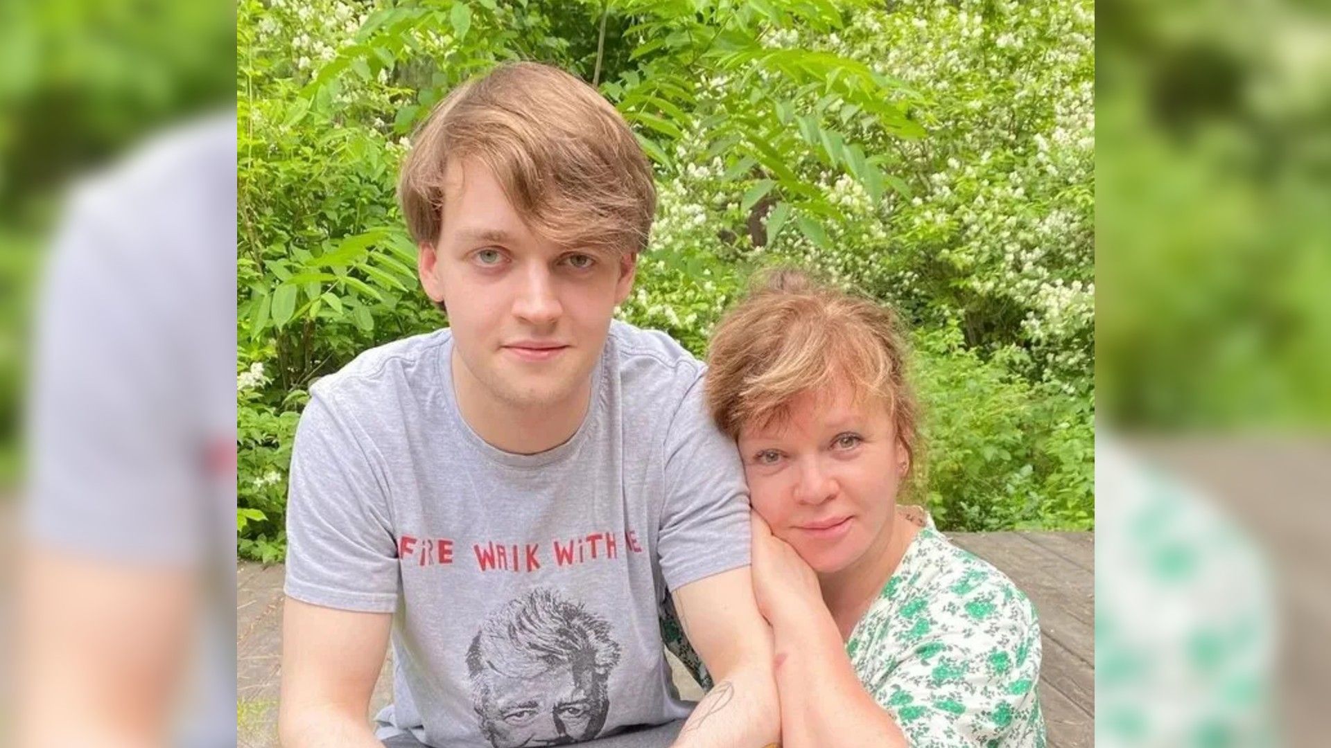 Елена Валюшкина и её сын Василий и молодой человек позируют на фоне зелёных кустов, сидя рядом на деревянной террасе