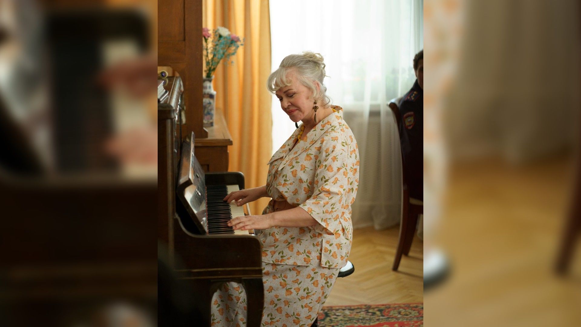 Елена Валюшкина в цветочном костюме играет на пианино в уютной комнате с мягким освещением