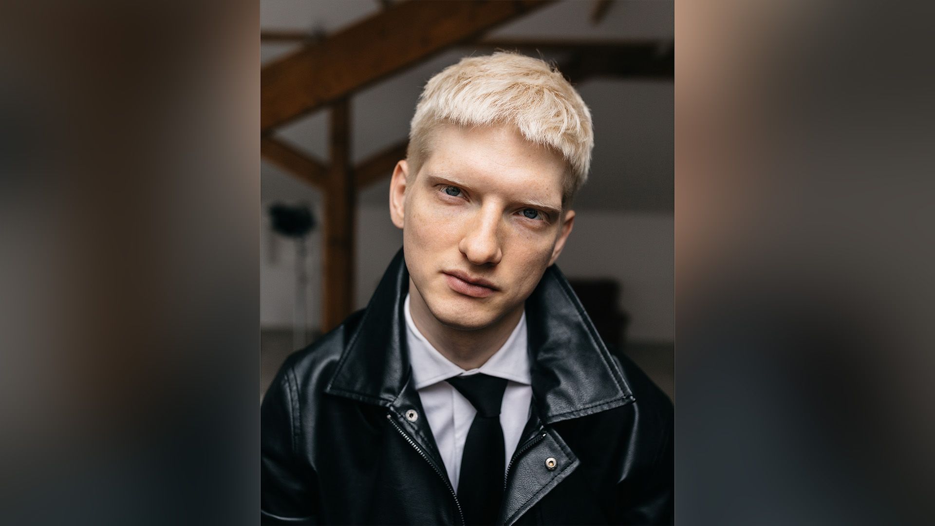 Святослав Рогожан в черной кожаной куртке, белой рубашке и галстуке смотрит в камеру