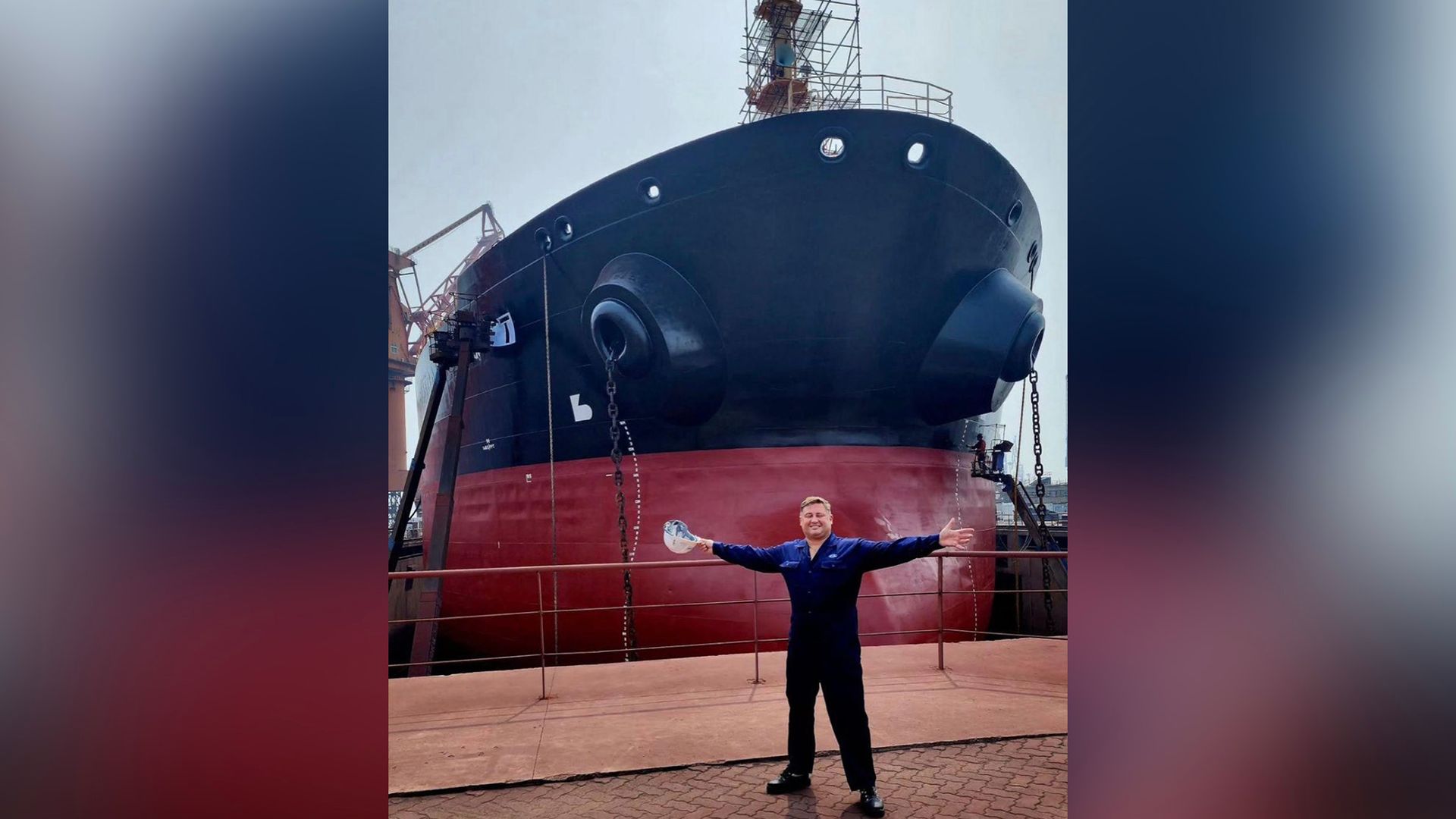 Алексей Халявин стоит на фоне морского судна, раскинув руки